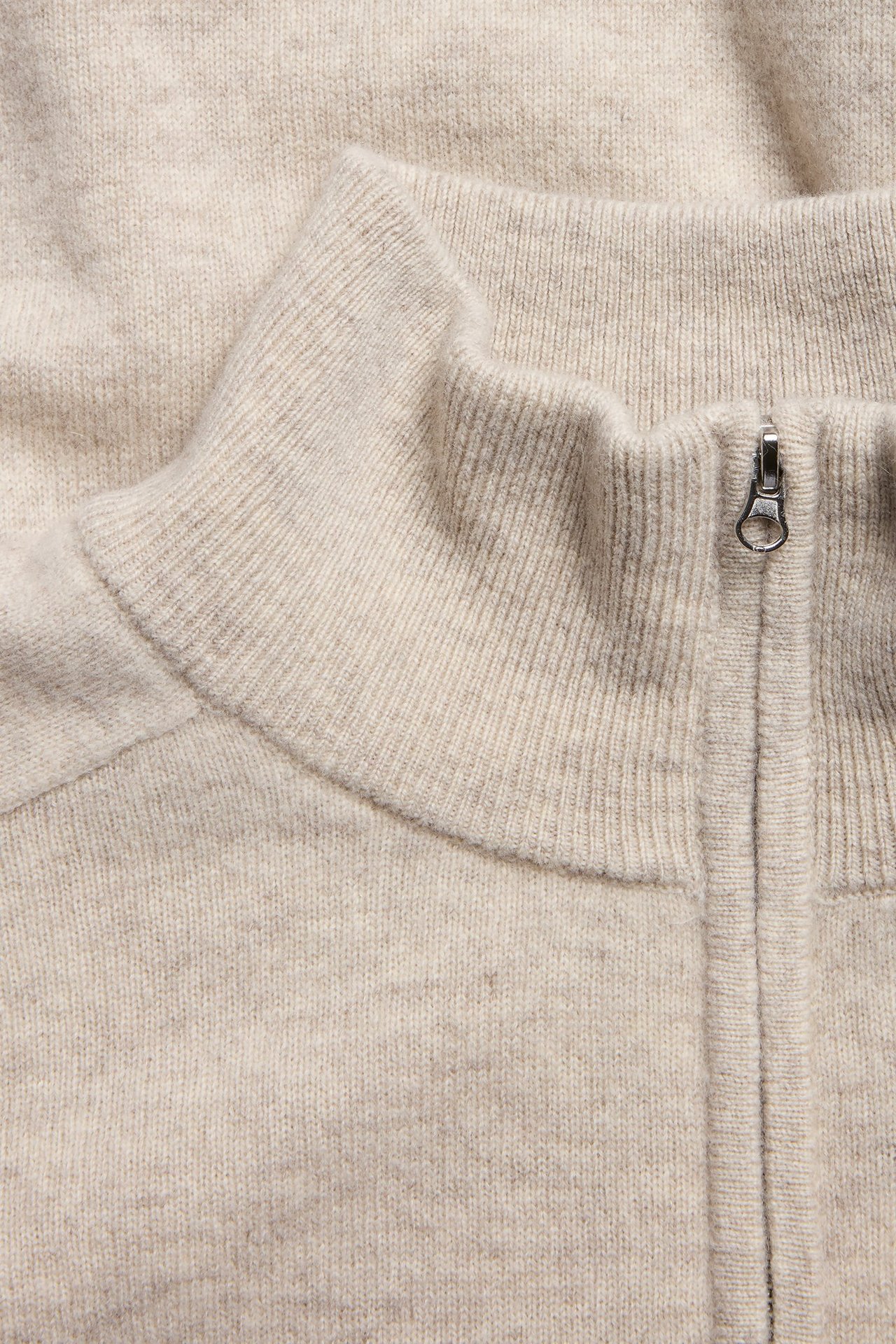 Zbliżenie beżowego melanżowego swetra wełnianego z półzamkiem, prążkowanym kołnierzem i srebrnym zamkiem.