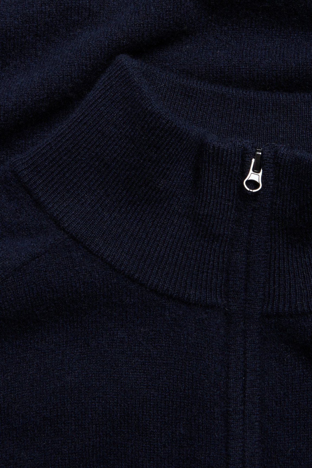 Zbliżenie na ciemnoniebieski wełniany sweter half-zip ze srebrnym zamkiem przy kołnierzu.