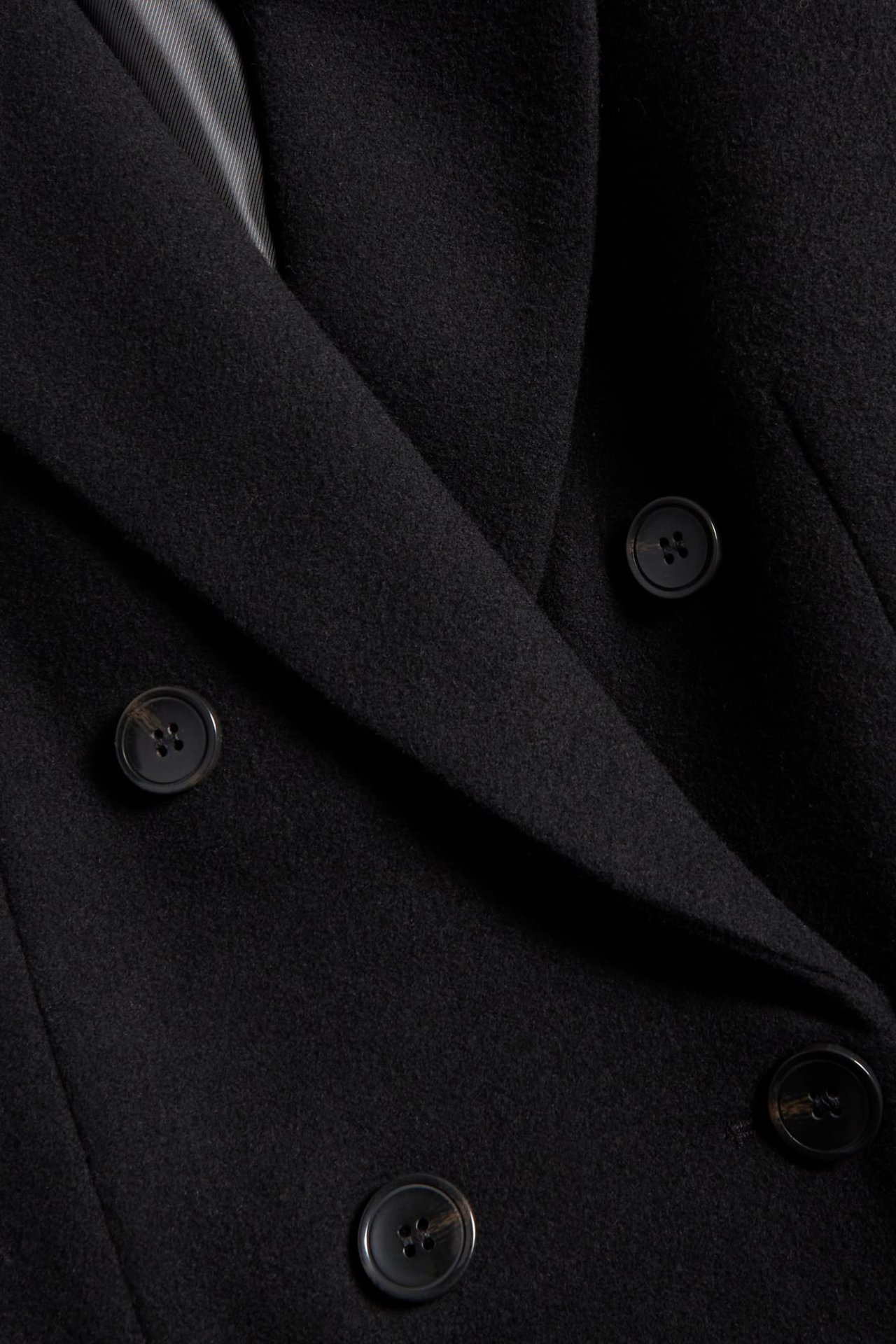 Zbliżenie czarnego długiego płaszcza z widocznymi guzikami i klapami.