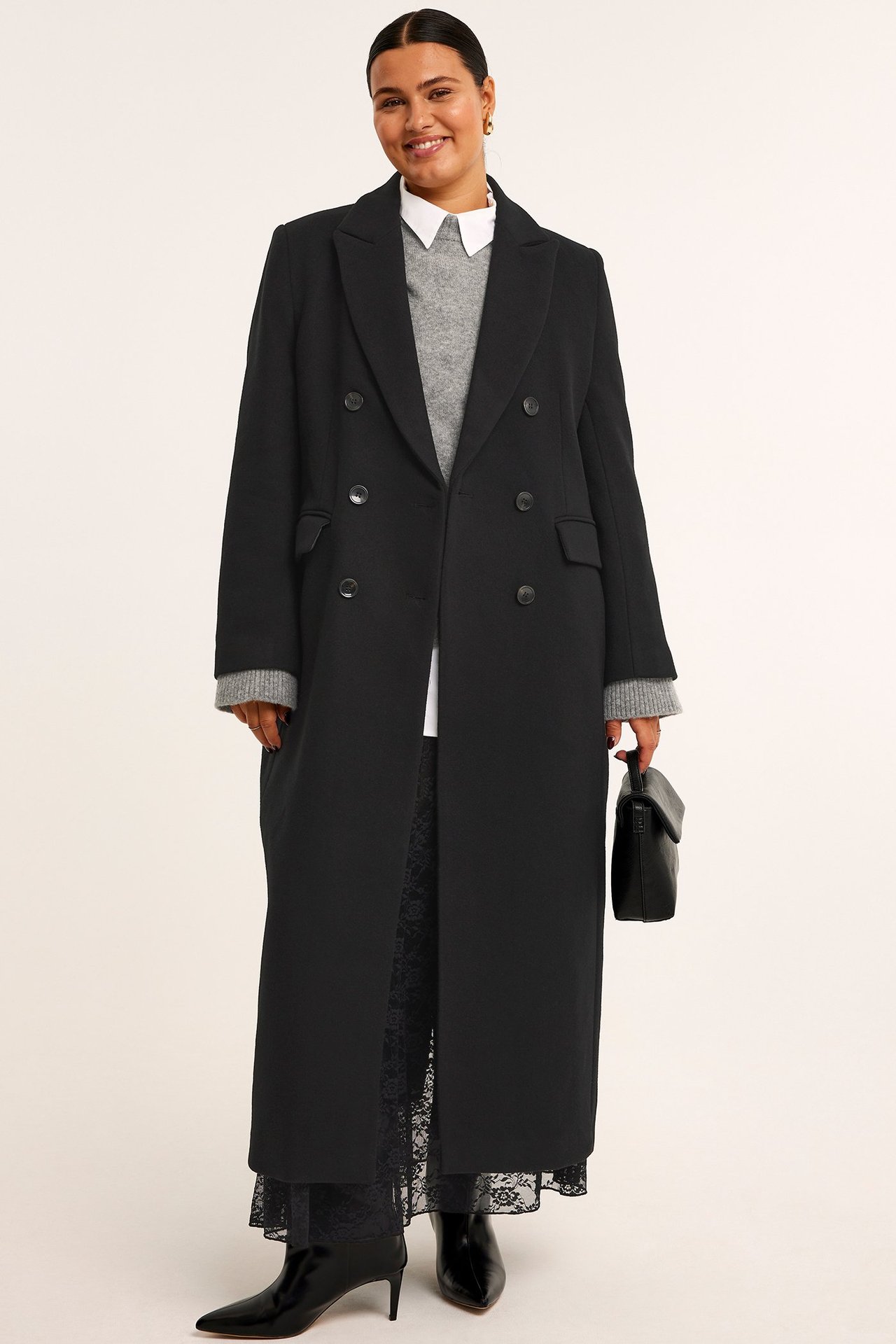 Długi czarny płaszcz dwurzędowy na szarym swetrze, koronkowych spodniach i czarnych botkach.