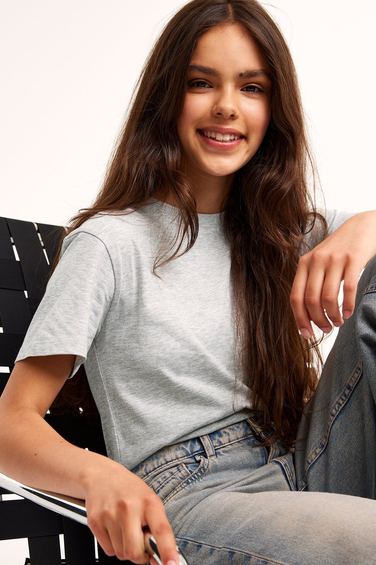 Framifrån, leende barn i en ljusgrå melerad t-shirt i bomullsblandning och ljusblå jeans.
