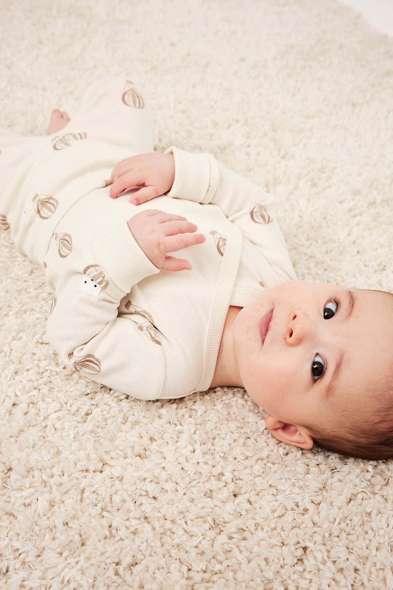 Ylhäältä: vauva beigessä ribatussa kietaisubodyssa, jossa ruskea kuumailmapallokuvio.