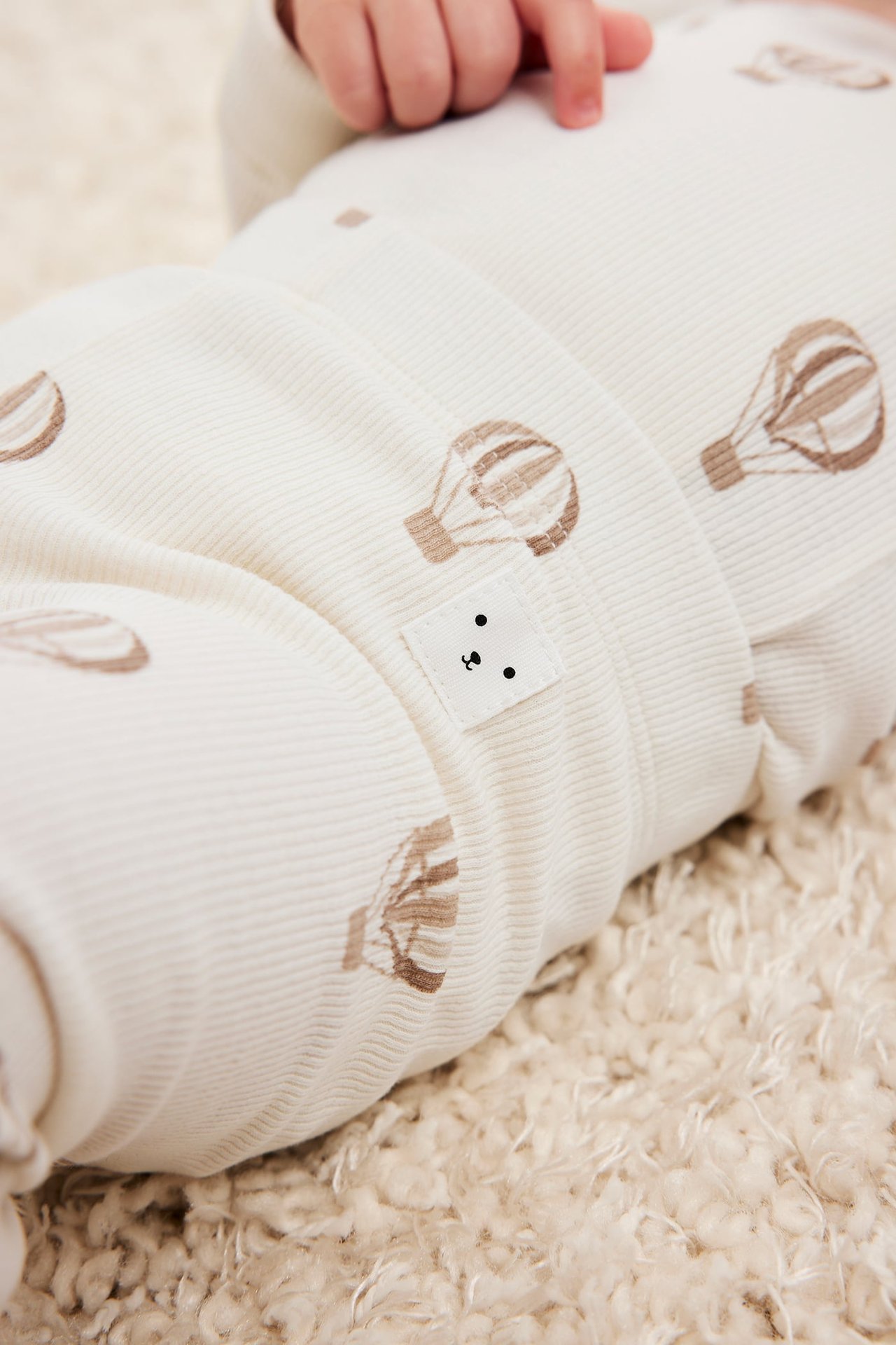 Nærbilde av baby i beige ribbestrikkede leggings med brunt luftballongmønster og liten bjørneetikett.