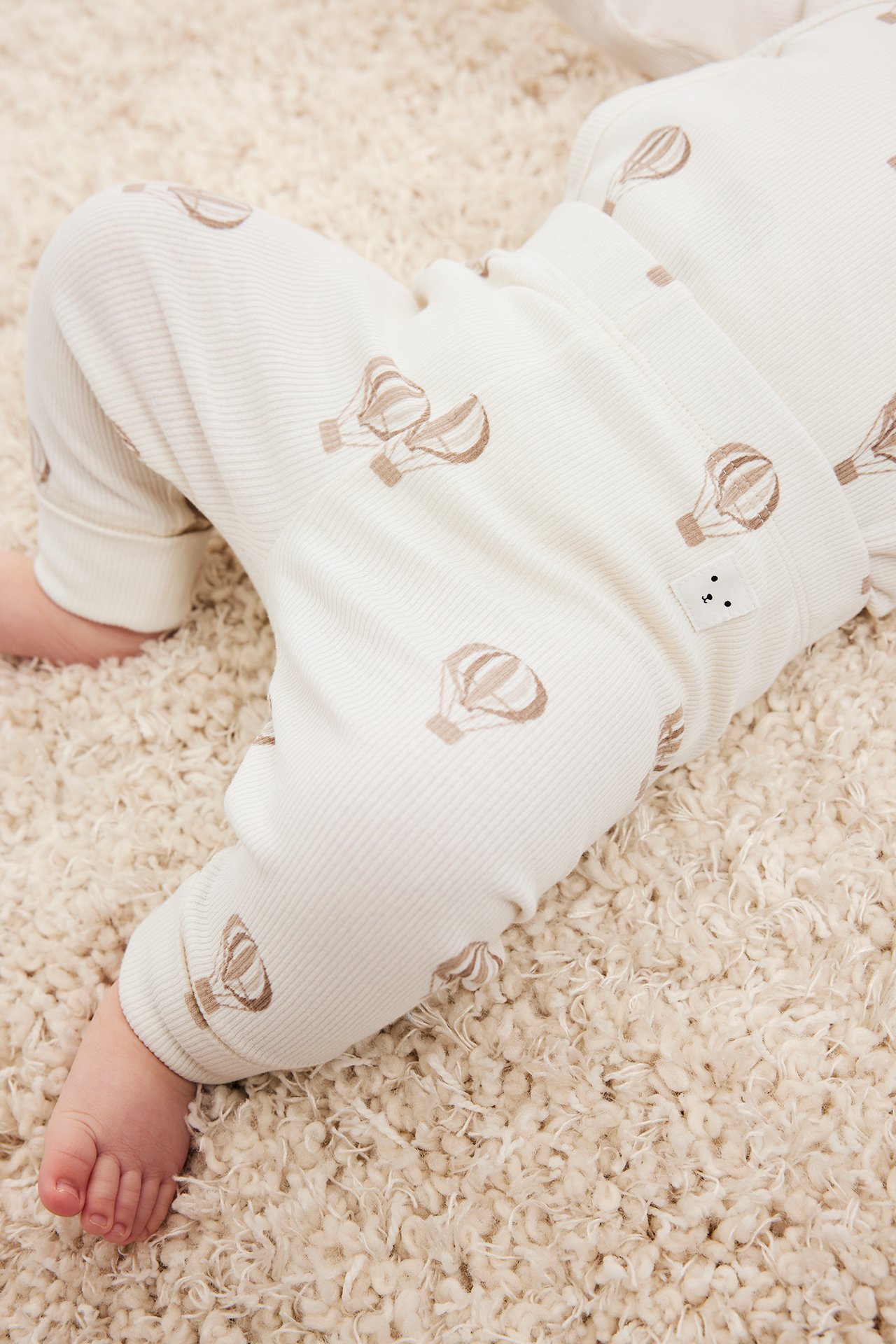 Närbild på baby i beige ribbade leggings med brunt luftballongsmönster och uppvikta muddar.