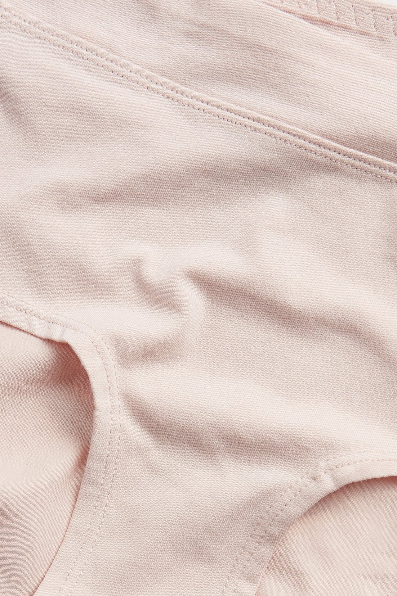 Lähikuva vaaleanpunaisista hipster-alushousuista pehmeää puuvillasekoitetta, leveällä vyötärönauhalla.