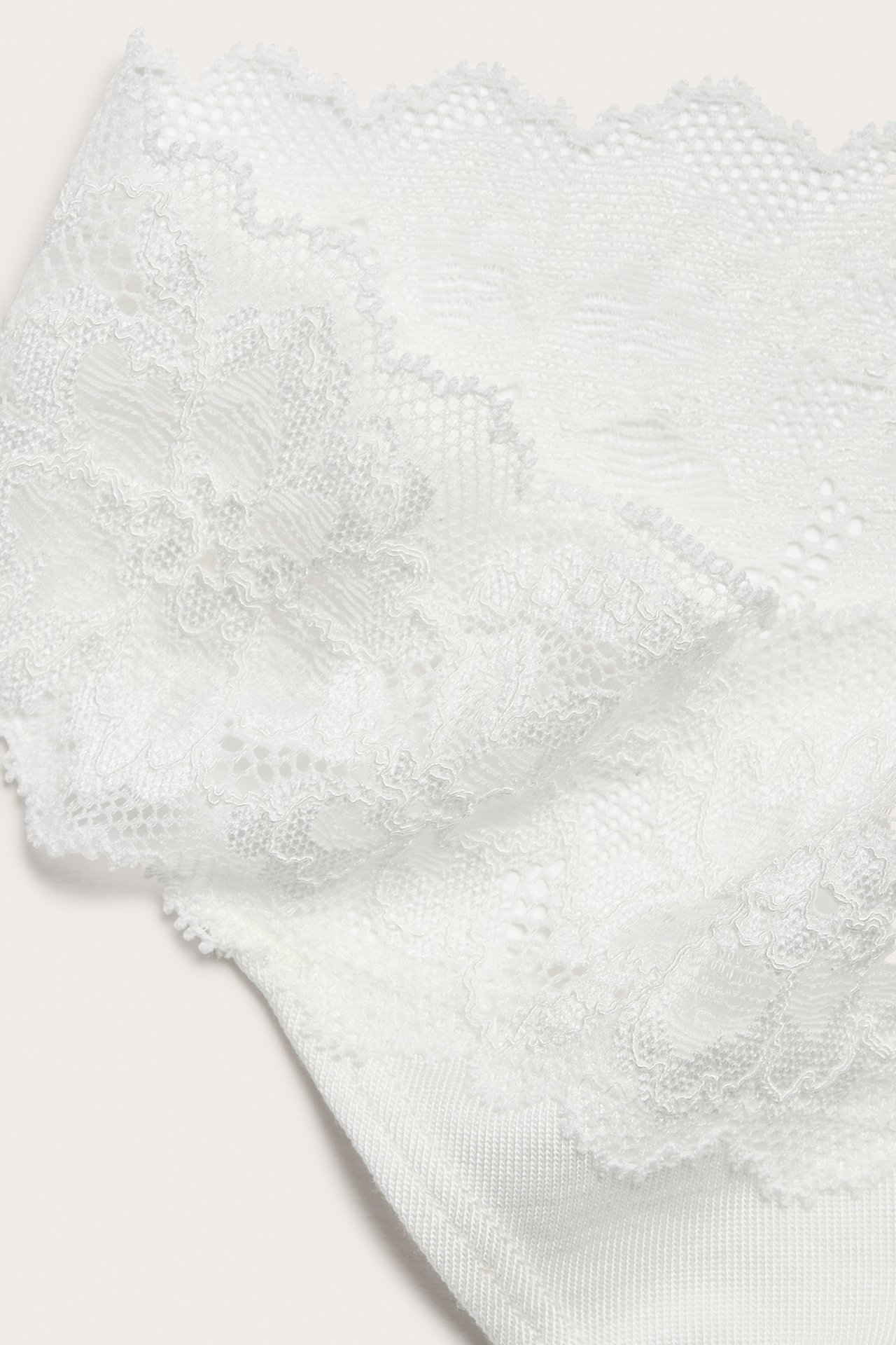 Nærbilde av en hvit lyocell stringtruse med en delikat blondekant.