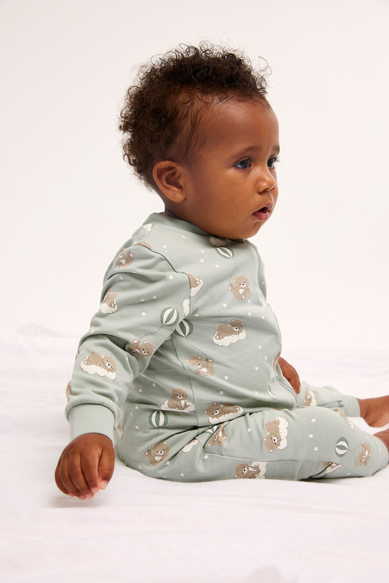 Sidovy av en baby i ljusgrön mönstrad pyjamas med björnar, moln och stjärnor.