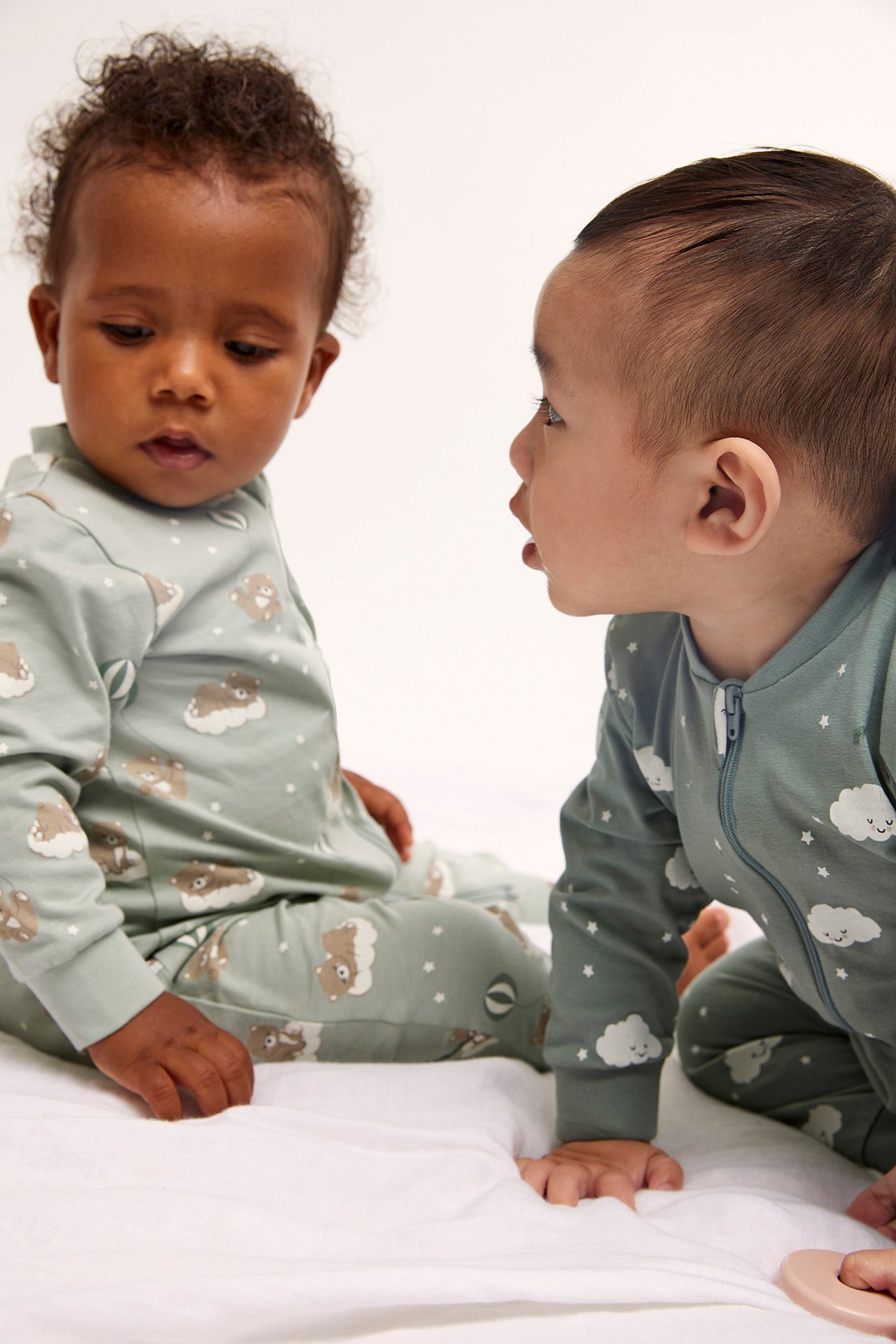 Sned framifrån-vy av två bebisar i ljusgröna mönstrade pyjamasar, en med får, en med moln och dragkedja.