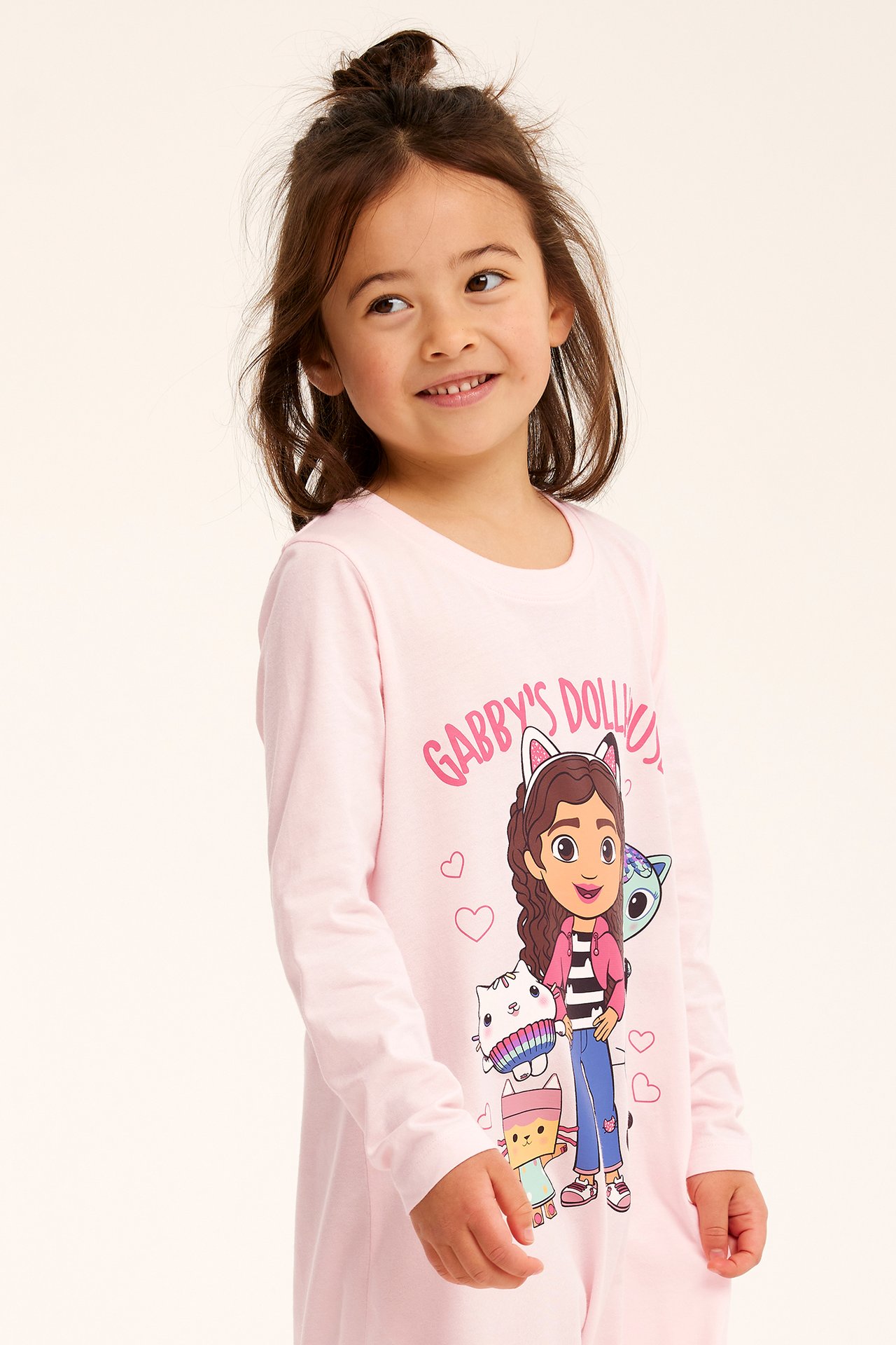 Framifrån, leende barn i ljusrosa långärmat nattlinne i bomull med Gabbys Dollhouse-tryck.