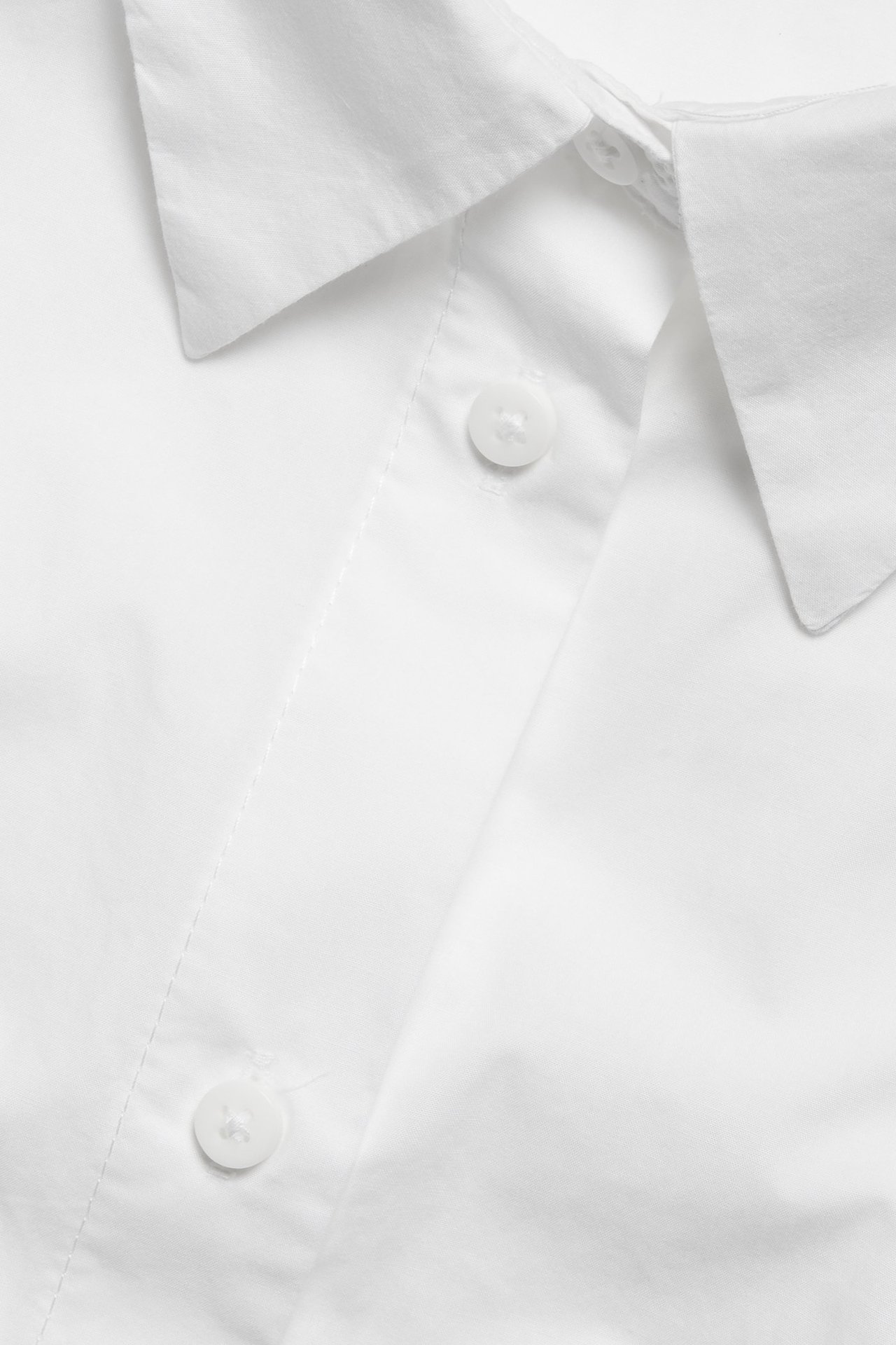 Zbliżenie białej koszuli oversize z popeliny bawełnianej z kołnierzykiem i białymi guzikami.