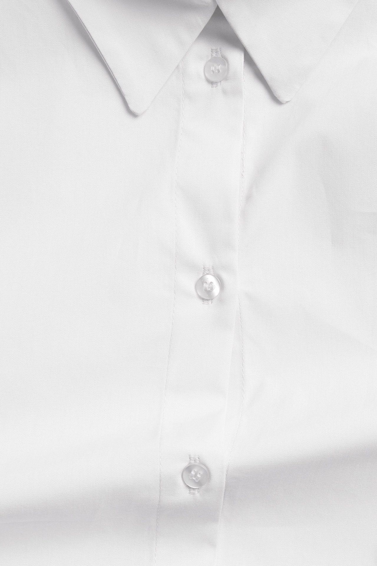Zbliżenie białej koszuli popelinowej oversize z klasycznym kołnierzykiem i białymi guzikami.