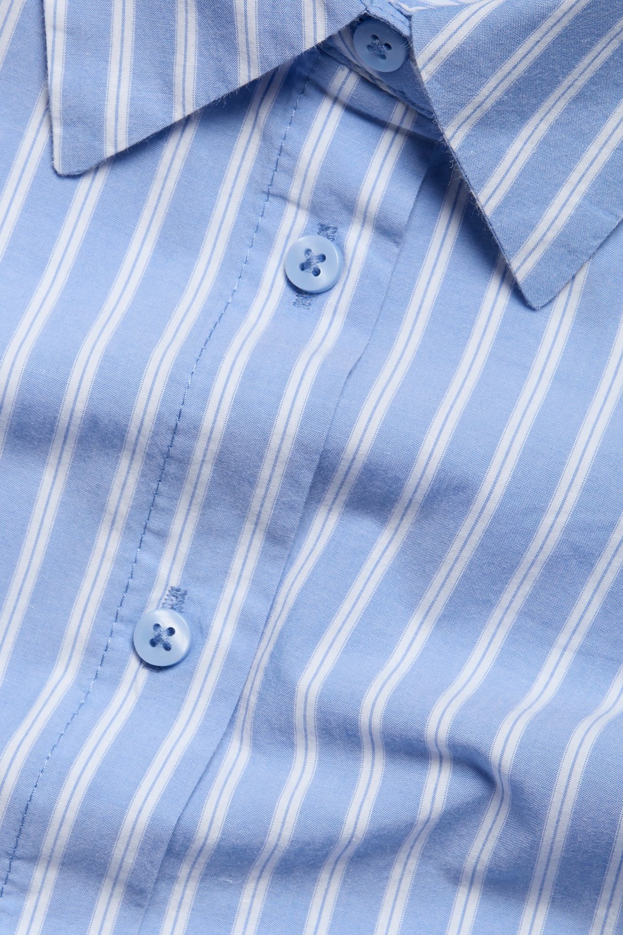Zbliżenie na niebiesko-białą, pasiastą koszulę oversize z popeliny bawełnianej z jasnoniebieskimi guzikami.