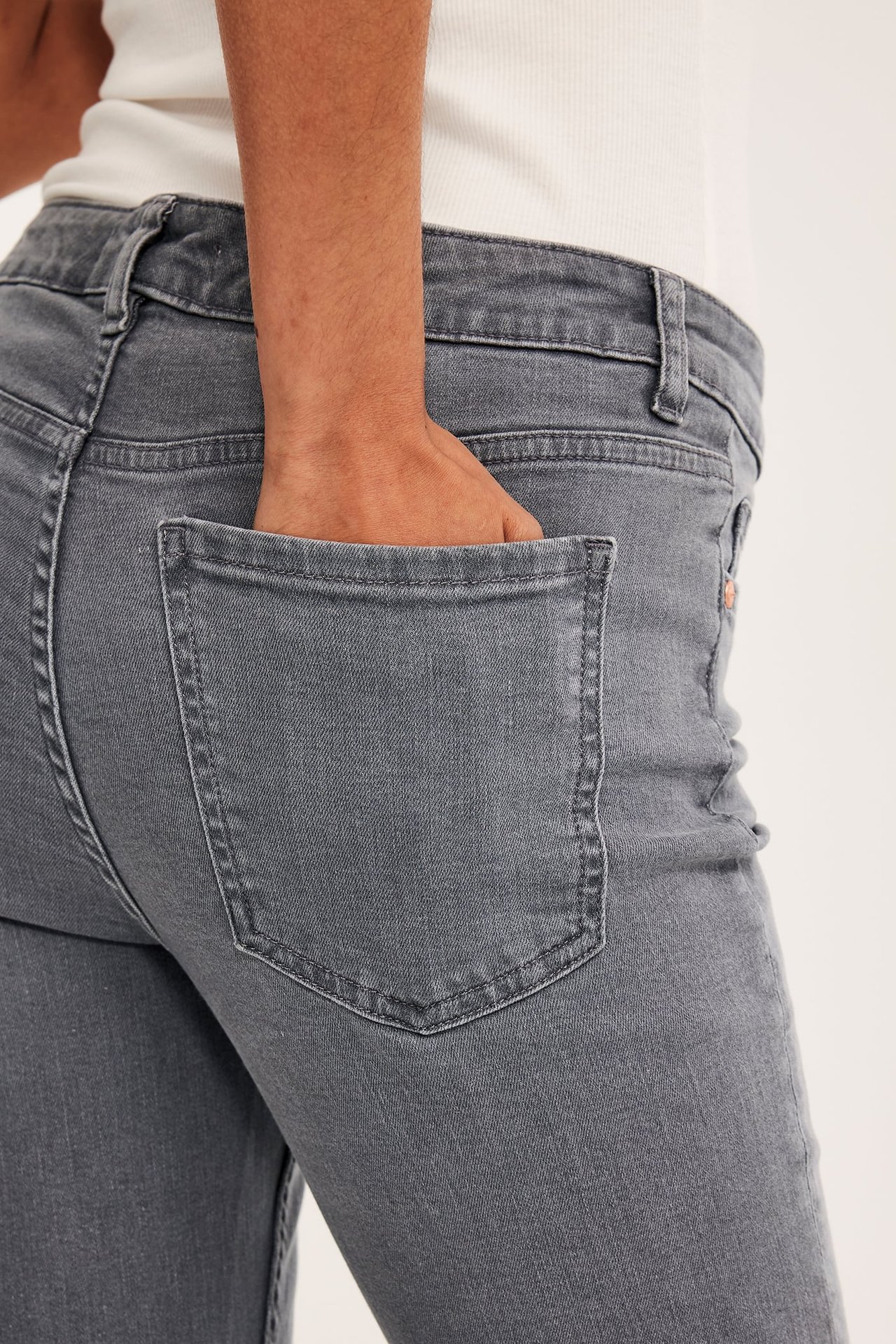 Närbild bakifrån på kvinna i lågmidjade grå bootcut-jeans, hand i fickan. Vit topp synlig.