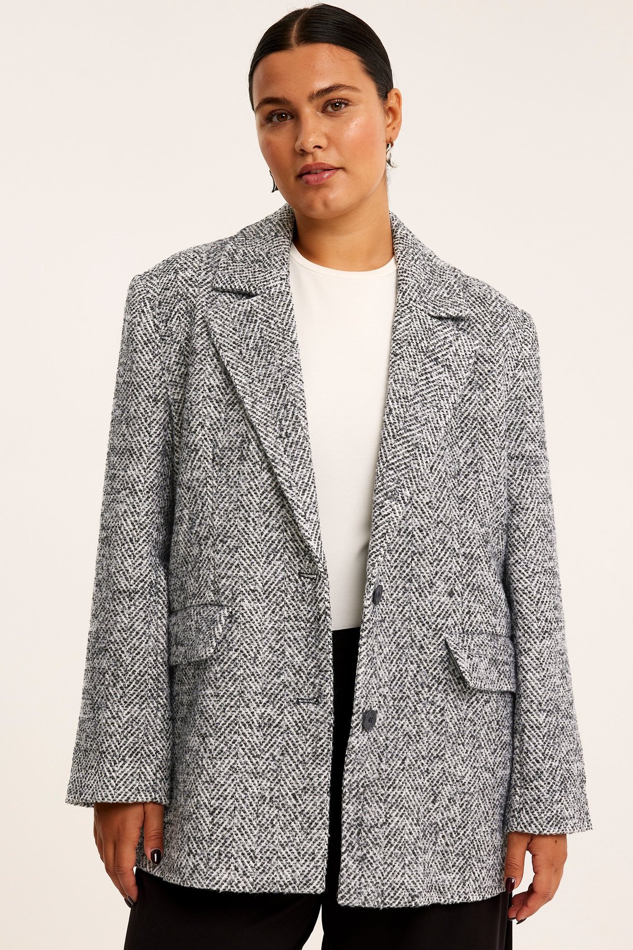 Edestä kuvattu nainen mustavalkoisessa tweedbleiserissä, valkoisen topin ja mustien housujen päällä.