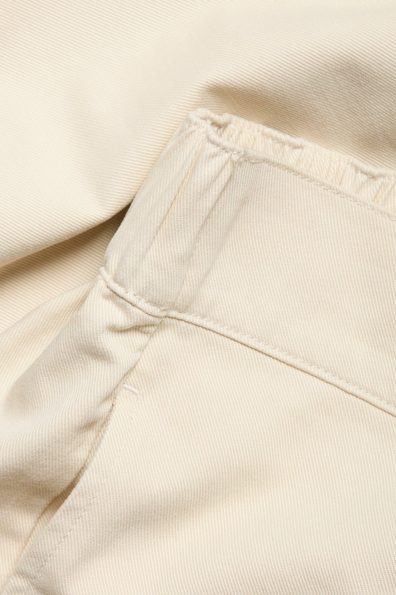 Zbliżenie jasnobeżowych spodni pull-on z elastycznym pasem i widoczną kieszenią boczną.