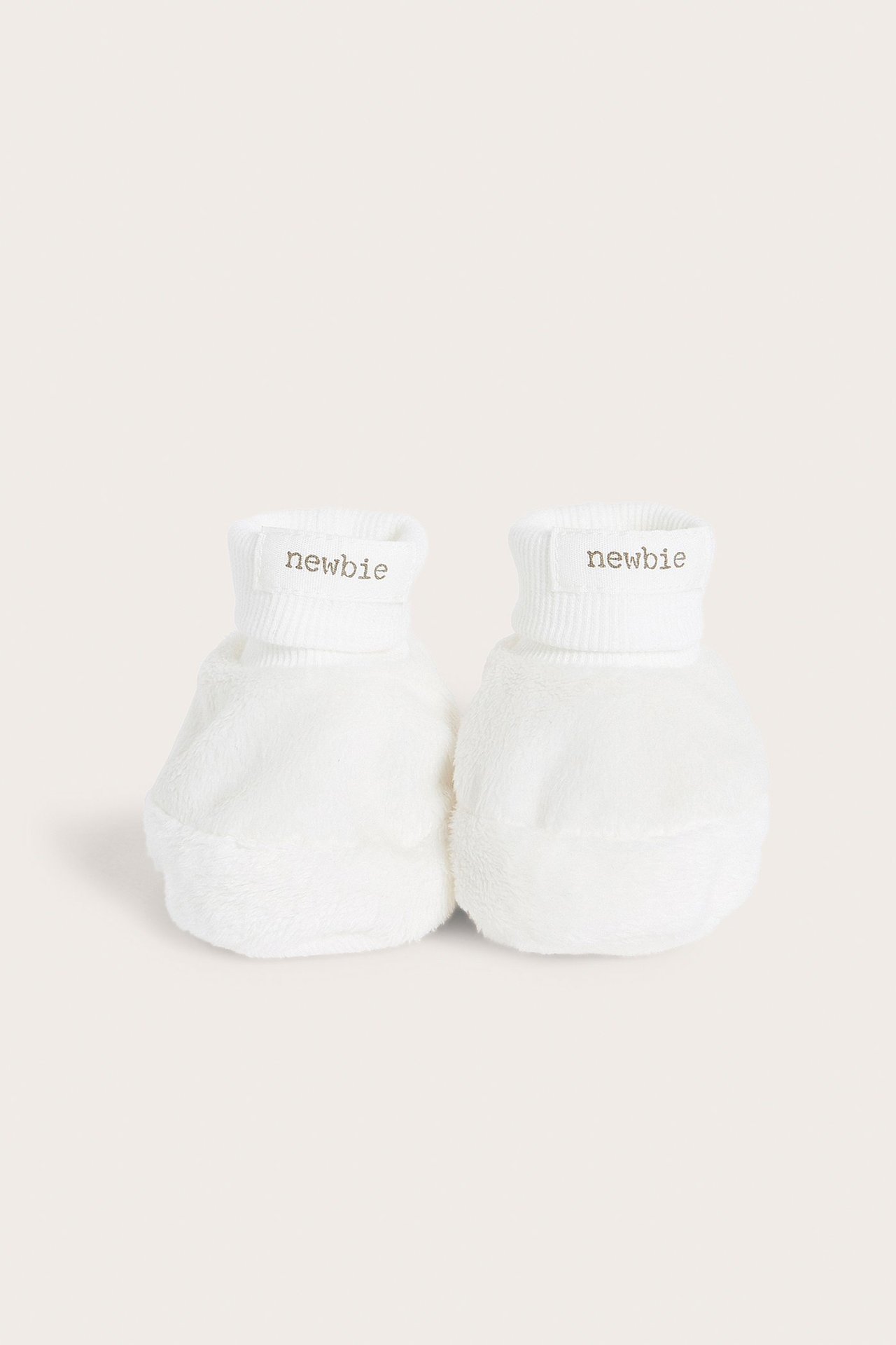Frontvy av ett par offwhite fluffiga babytossor med ribbade muddar och 'newbie'-etiketter.