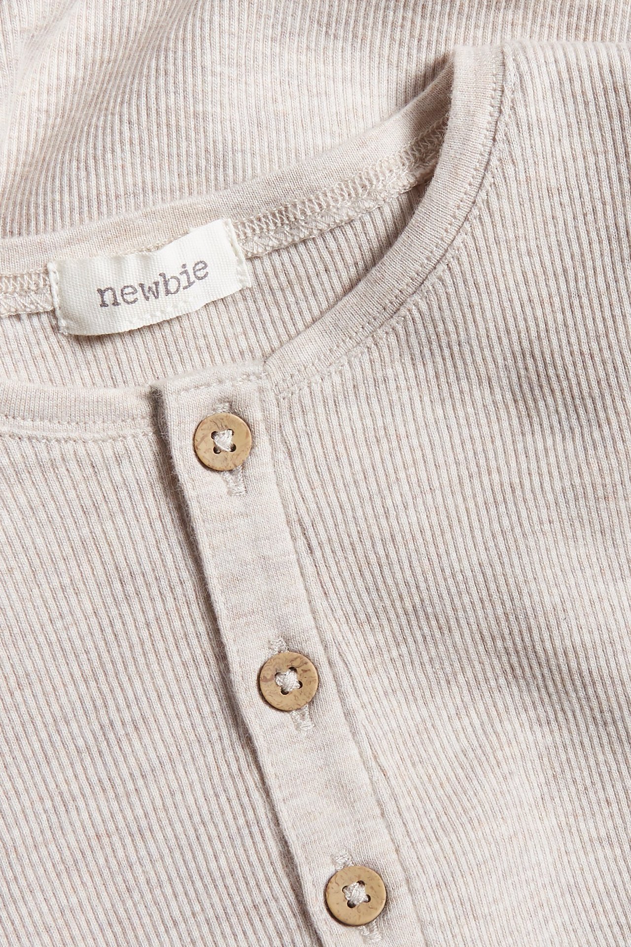 Närbild på en beige melerad ribbad långärmad babybody med träknappar på knappslån.