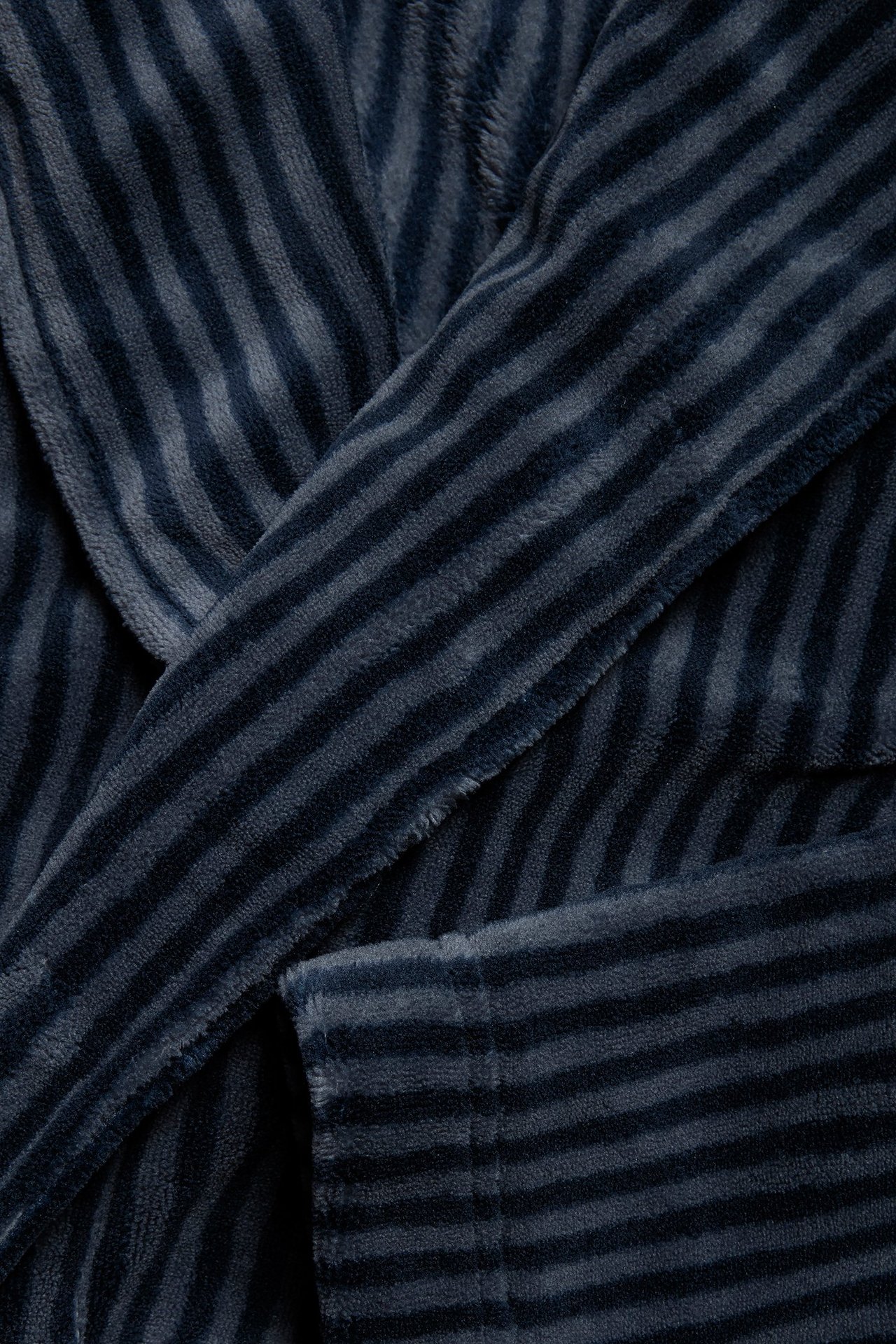 Zbliżenie na ciemnoniebieski, pasiasty męski szlafrok polarowy, pokazujące klapę i przednią kieszeń.