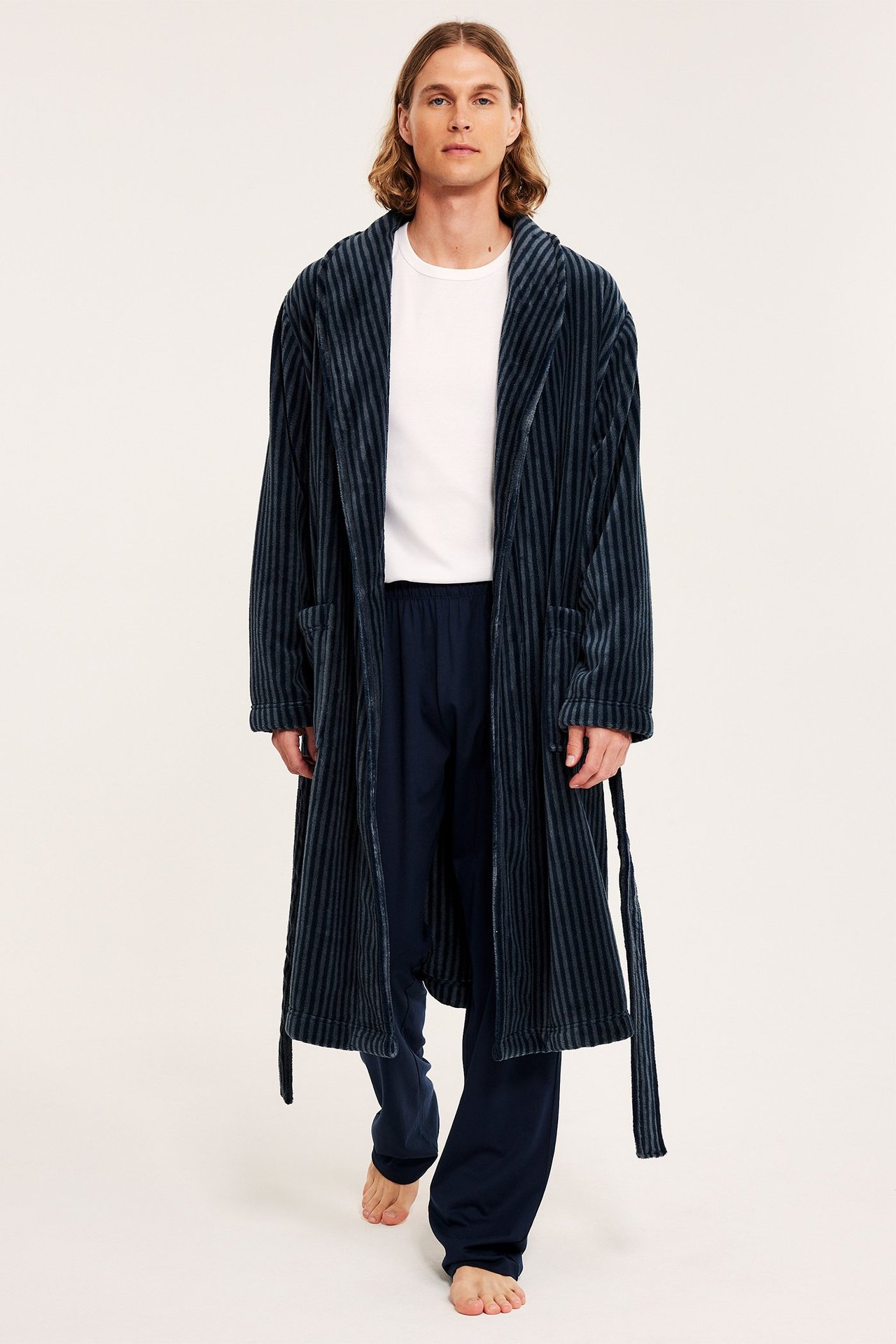 Edestäpäin, mies tummansinisessä raidallisessa fleece-aamutakissa, valkoisessa t-paidassa ja tummansinisissä housuissa.