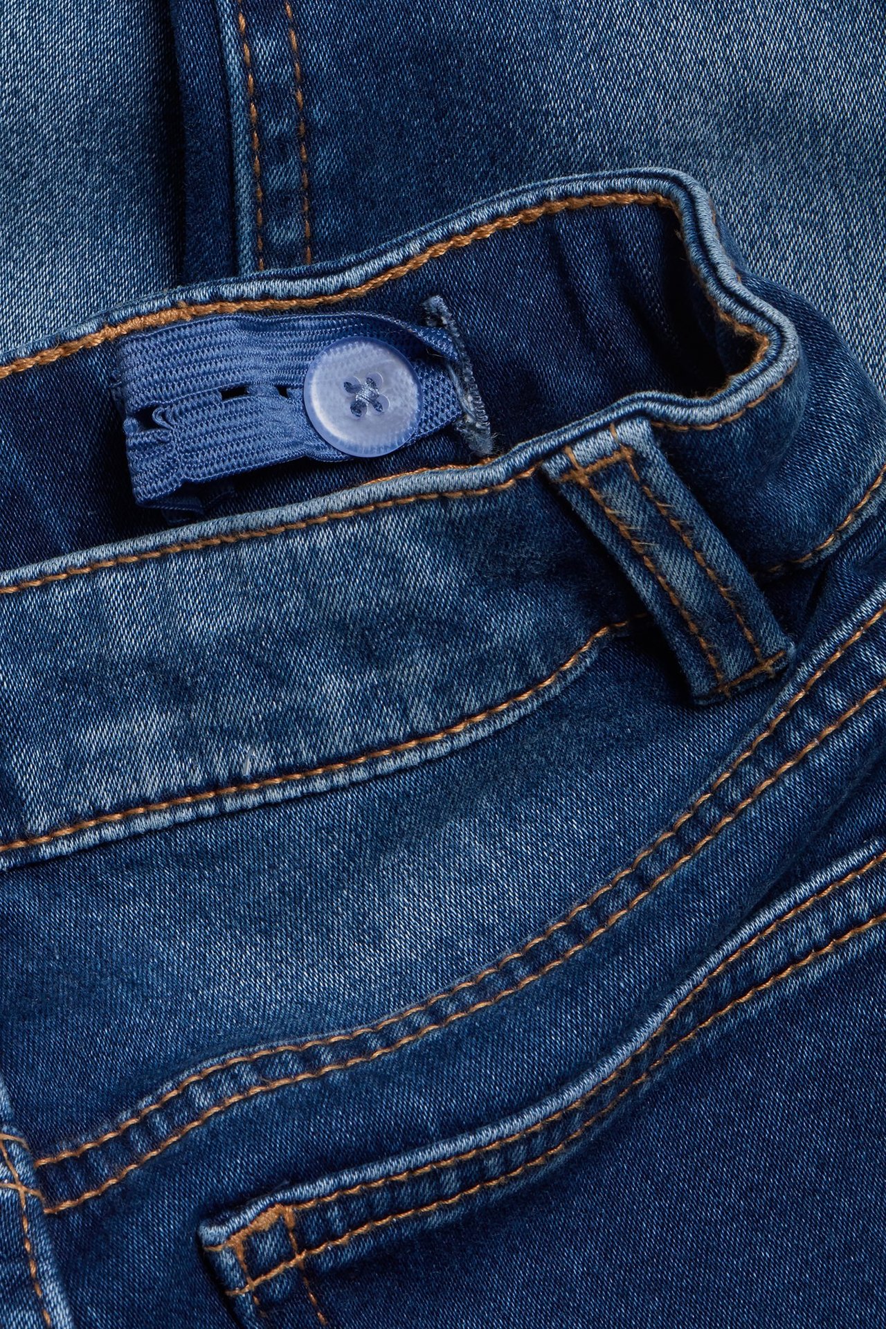 Lähikuva lasten tummansinisistä slim jogger-farkuista säädettävällä kuminauhavyötäröllä ja napilla.