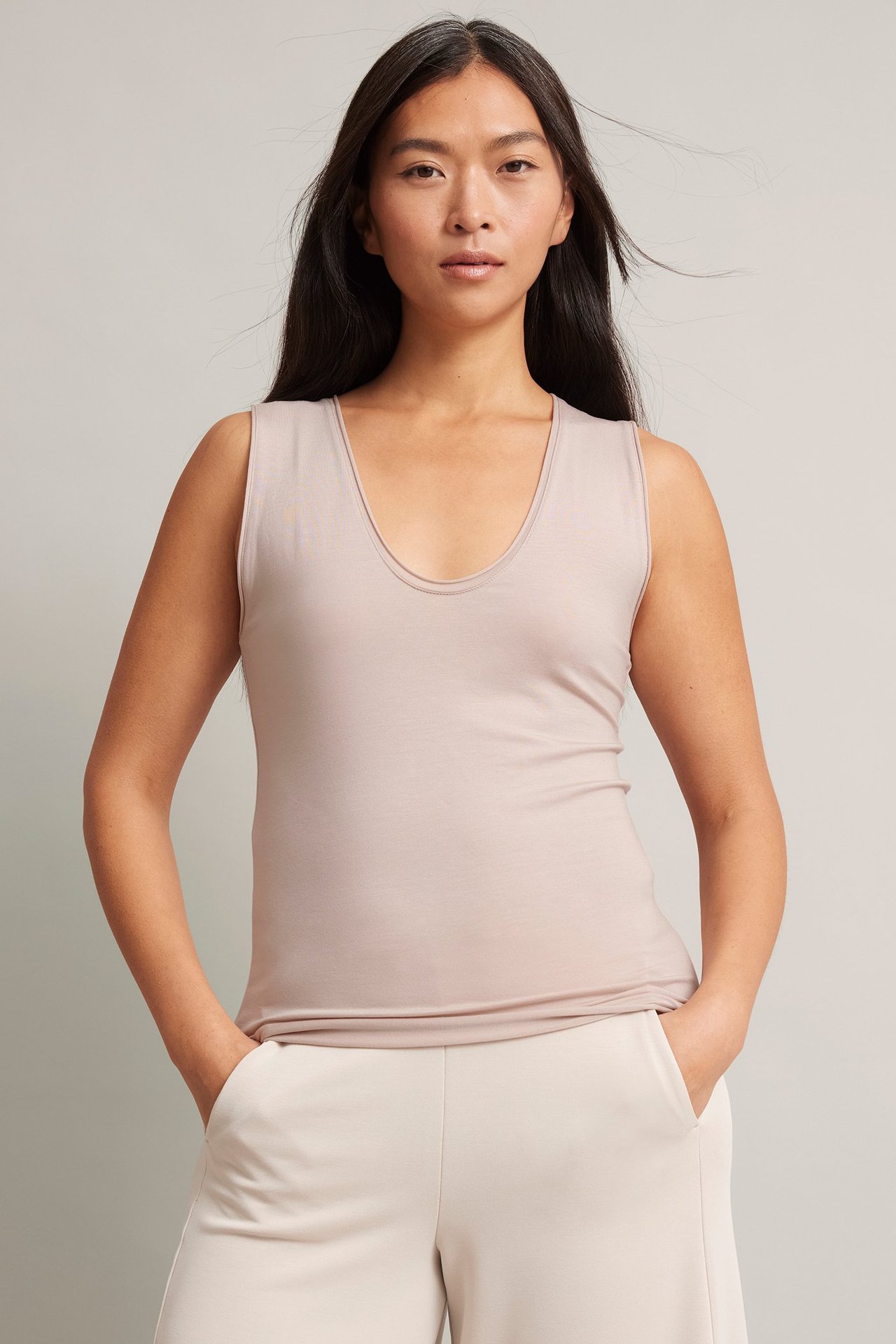 Frontbilde av en kvinne i en beige tanktopp av lyocellblanding og lysebeige vide bukser.