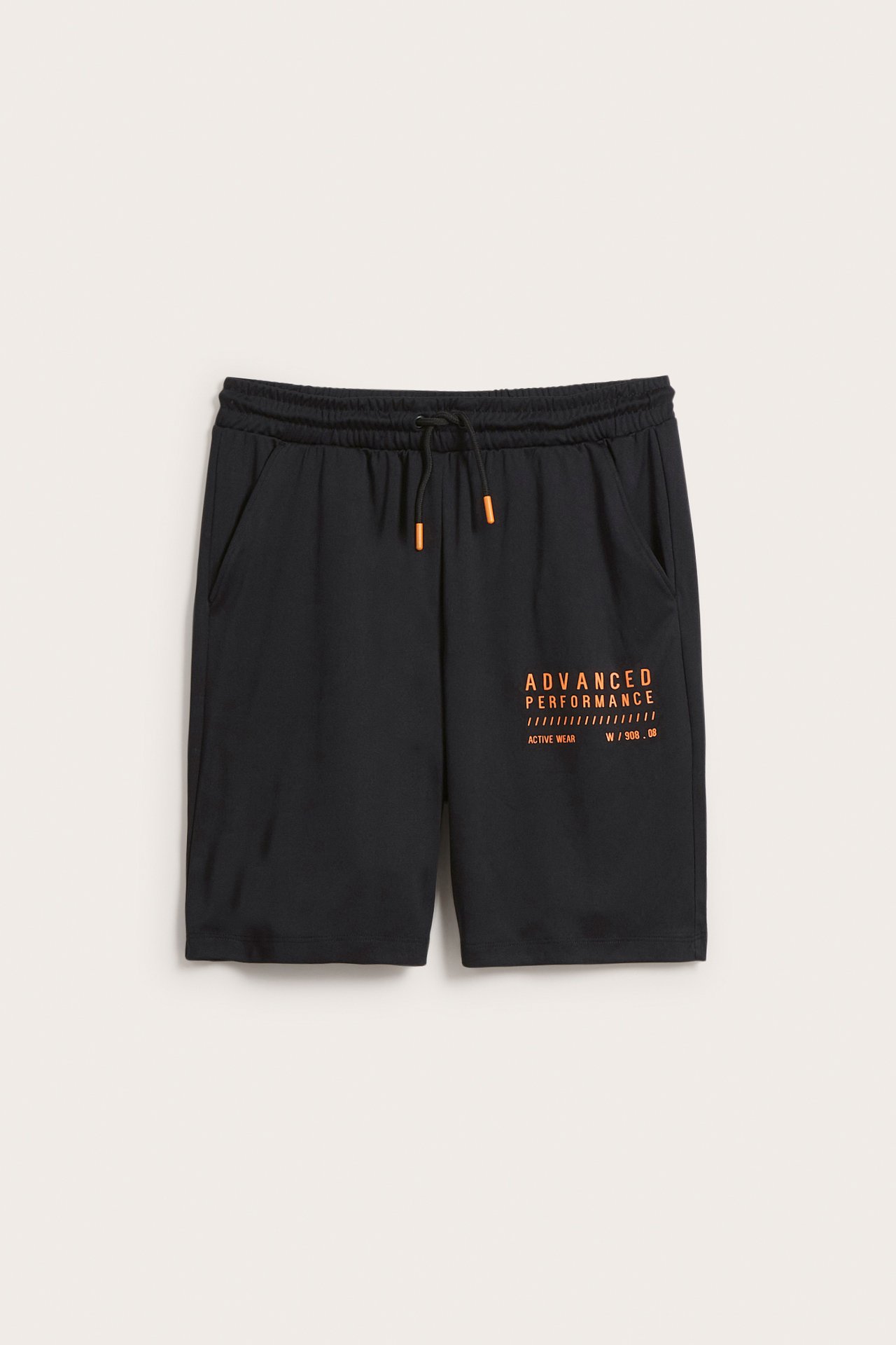 Framsida: svarta träning shorts för barn med orange tryck på vänster ben, orange dragsko i midjan.