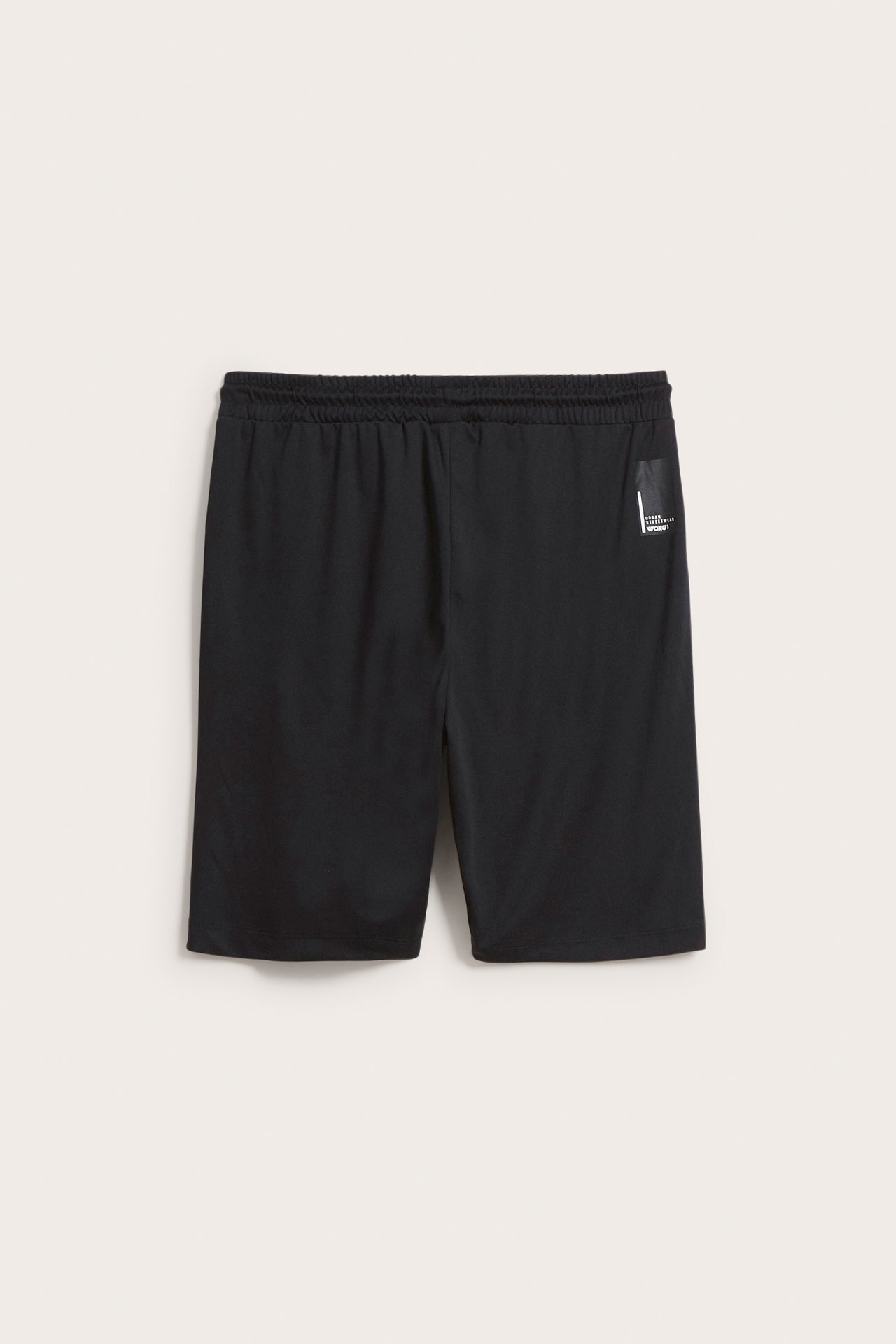 Framifrån svarta träningsshorts i polyester med resår i midjan och litet vitt tryck.