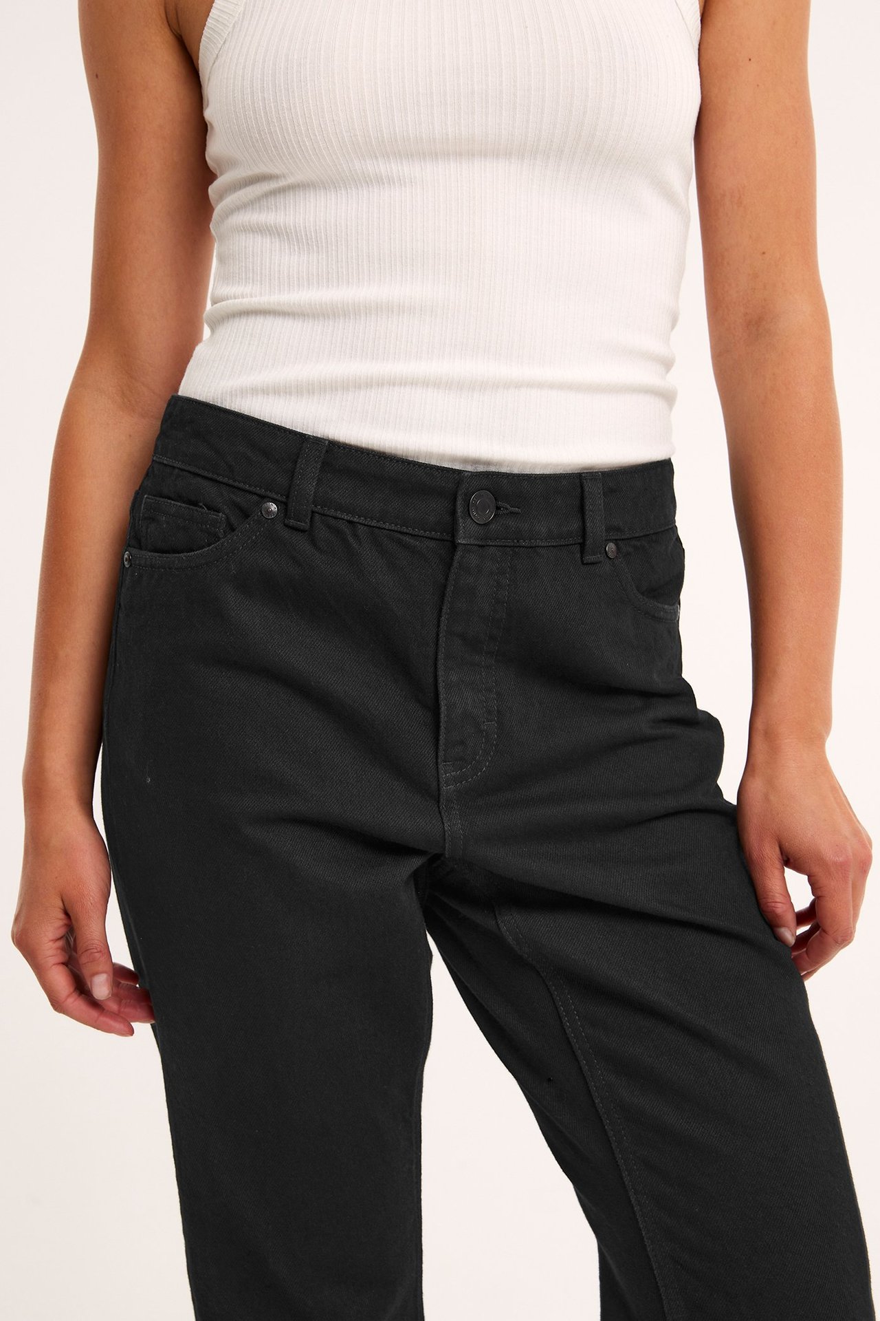 Frontvy av kvinna i svarta raka jeans med hög midja och vitt ribbat linne.
