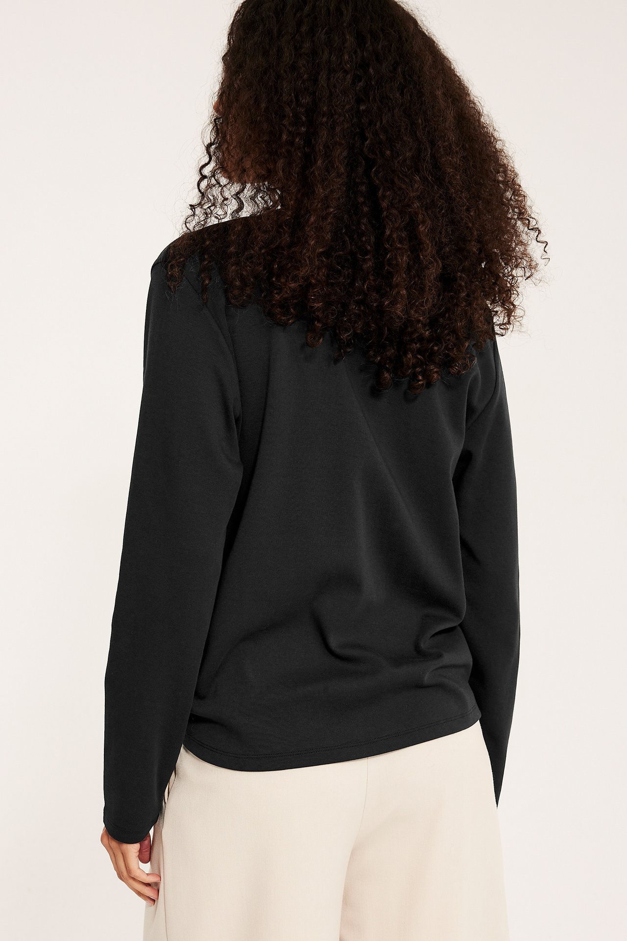 Widok z tyłu kobiety w czarnym, bawełnianym, długim rękawem topie basic i jasnobeżowych szortach.