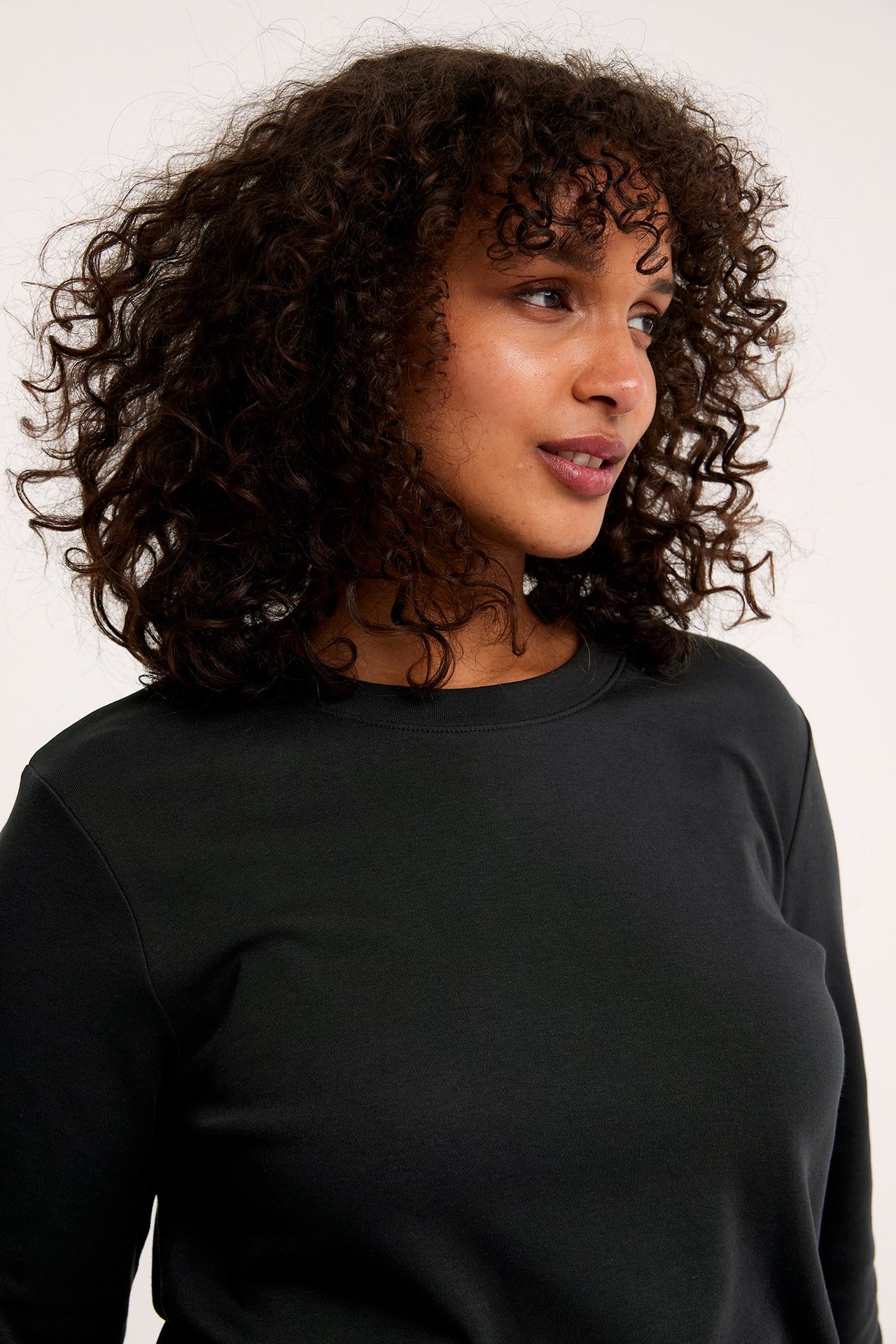 Nærbilde av en kvinne i en svart ensfarget langermet bomullstopp med rund hals.