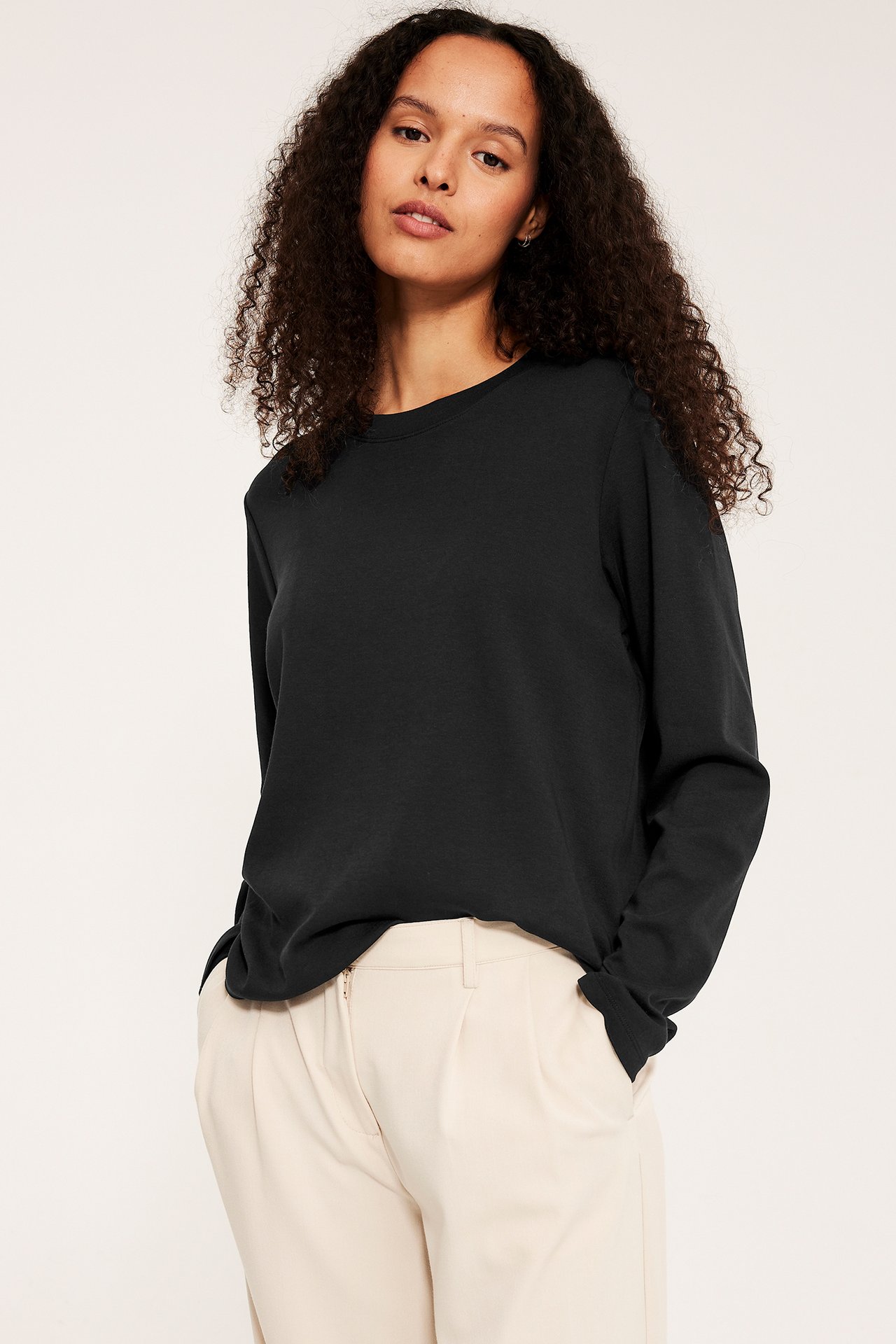 Widok z przodu: kobieta w czarnym bawełnianym topie z długim rękawem i beżowych spodniach w kant.