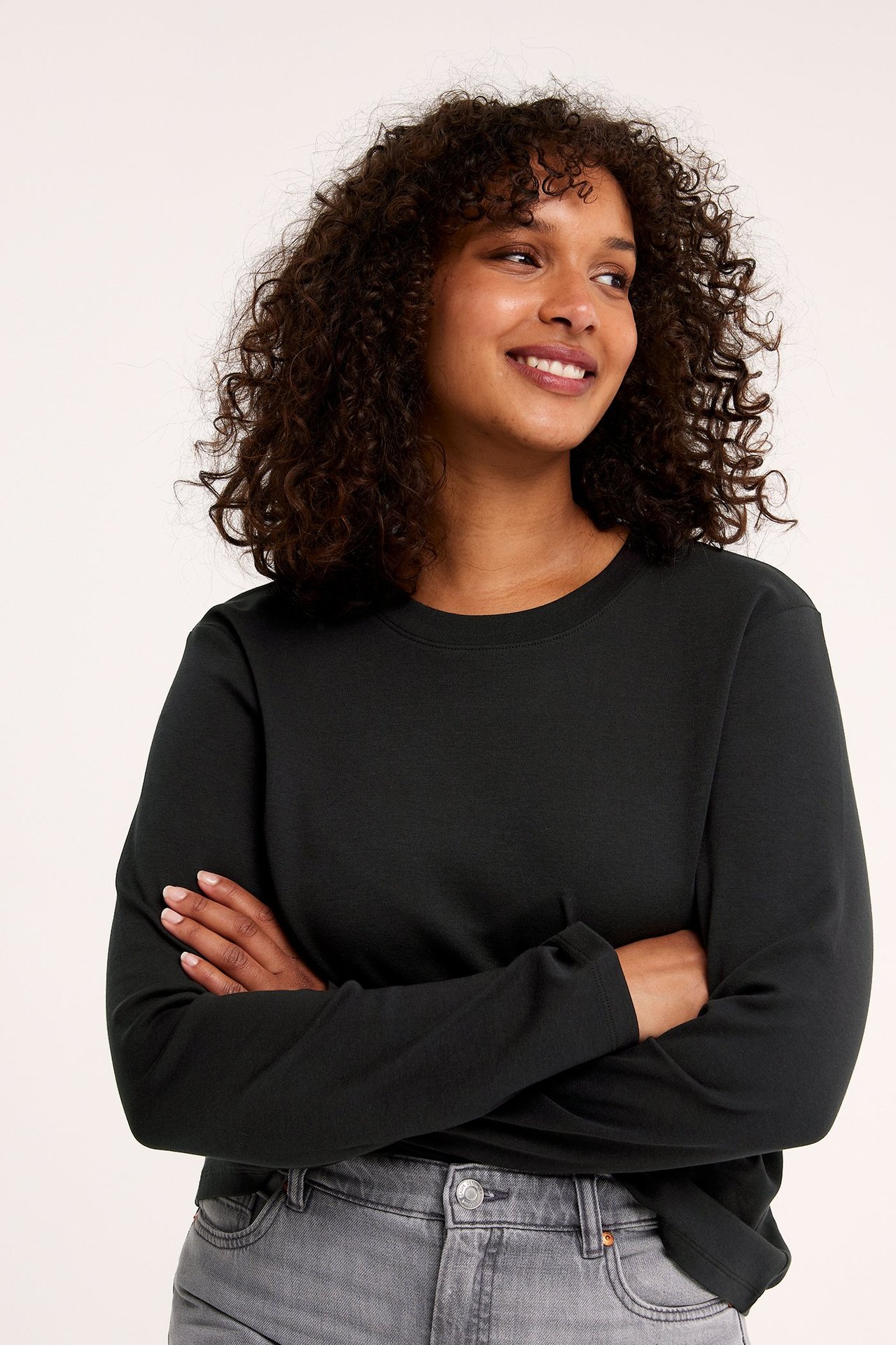 Frontbilde av en kvinne i en svart langermet bomulls-t-skjorte med rund hals og grå jeans.
