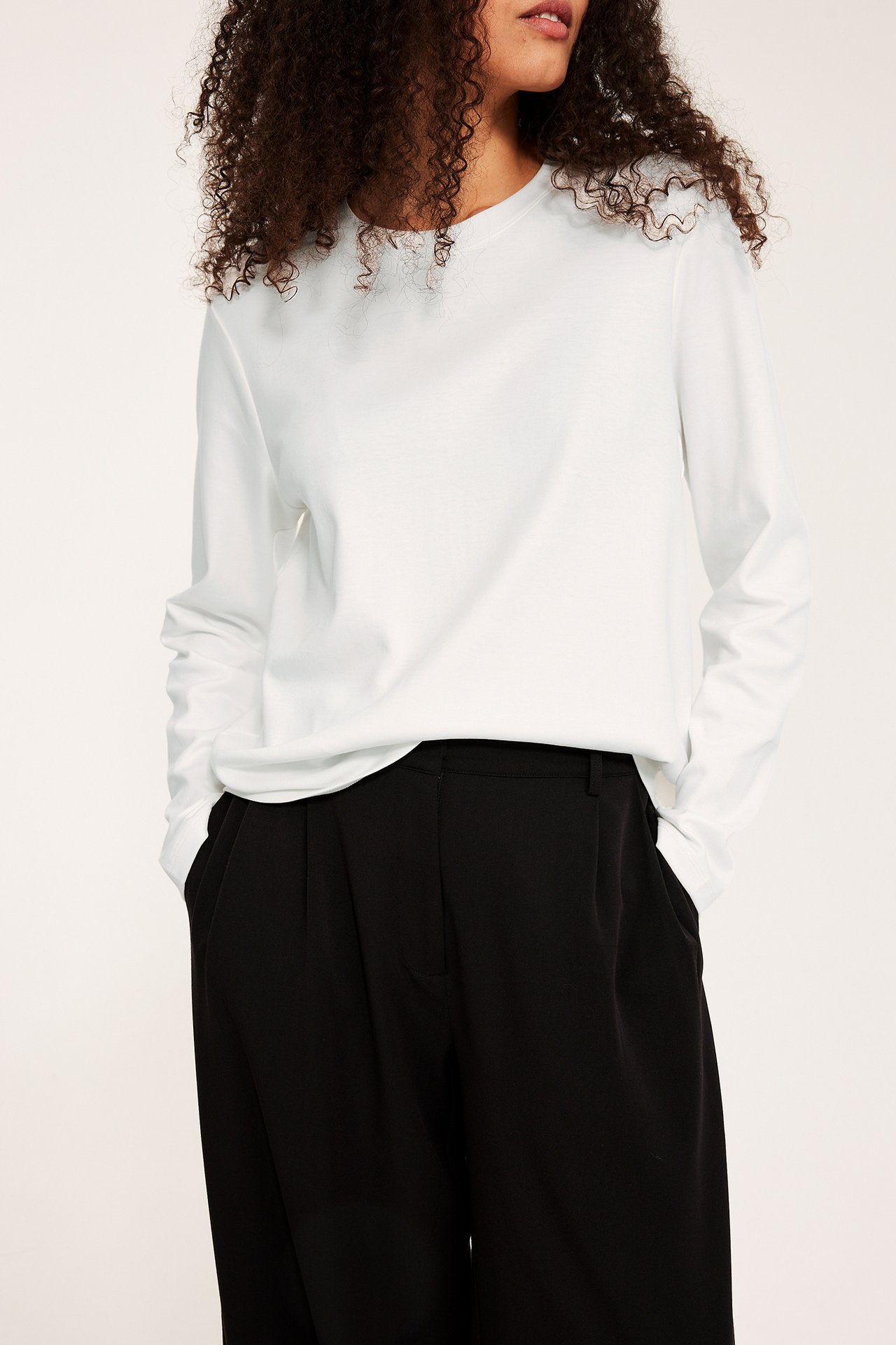 Naisen edestä näkymä: offwhite puuvillainen pitkähihainen toppi ja mustat laskoshousut.