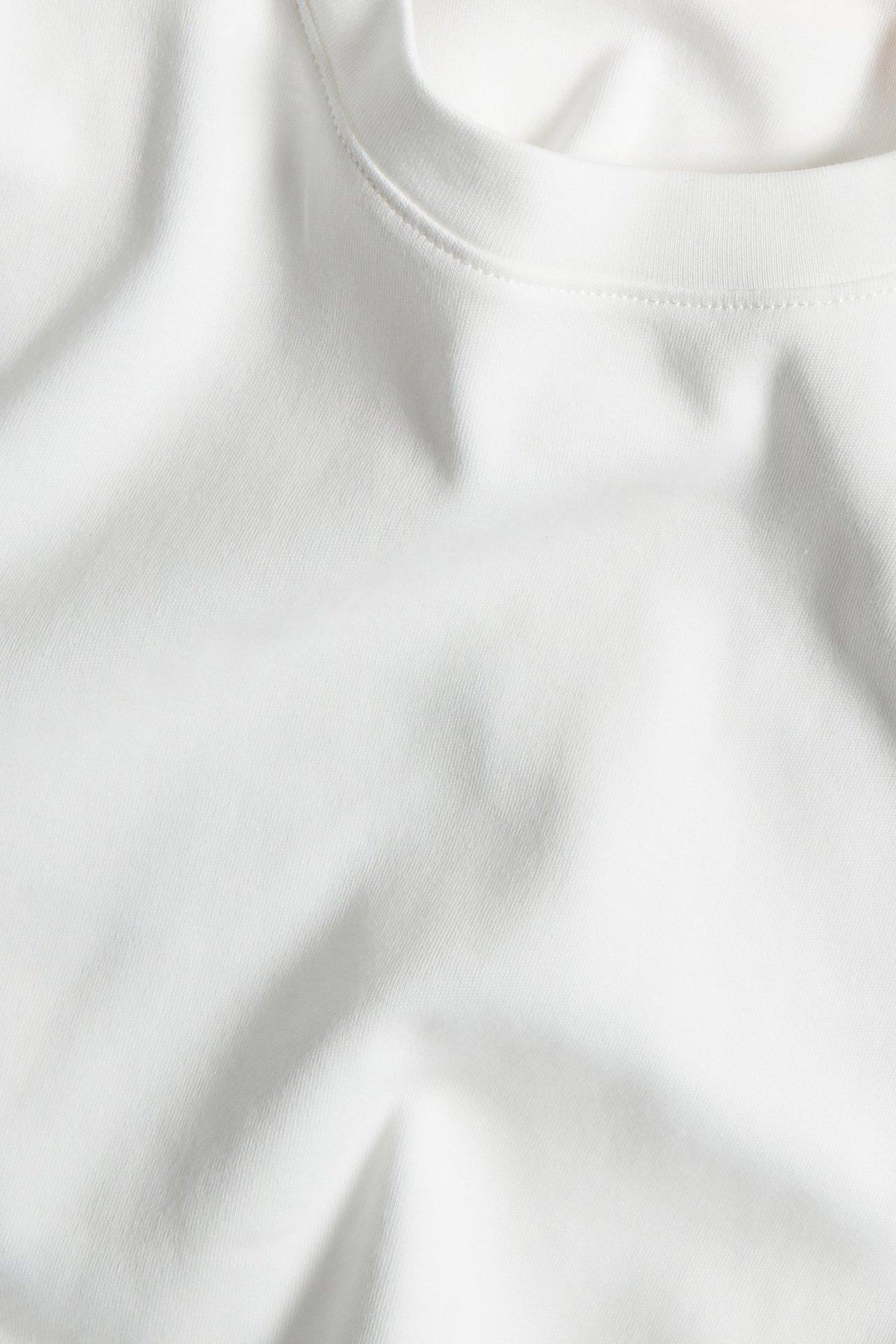 Zbliżenie na kremowy, jednolity, bawełniany t-shirt z długim rękawem i okrągłym dekoltem.
