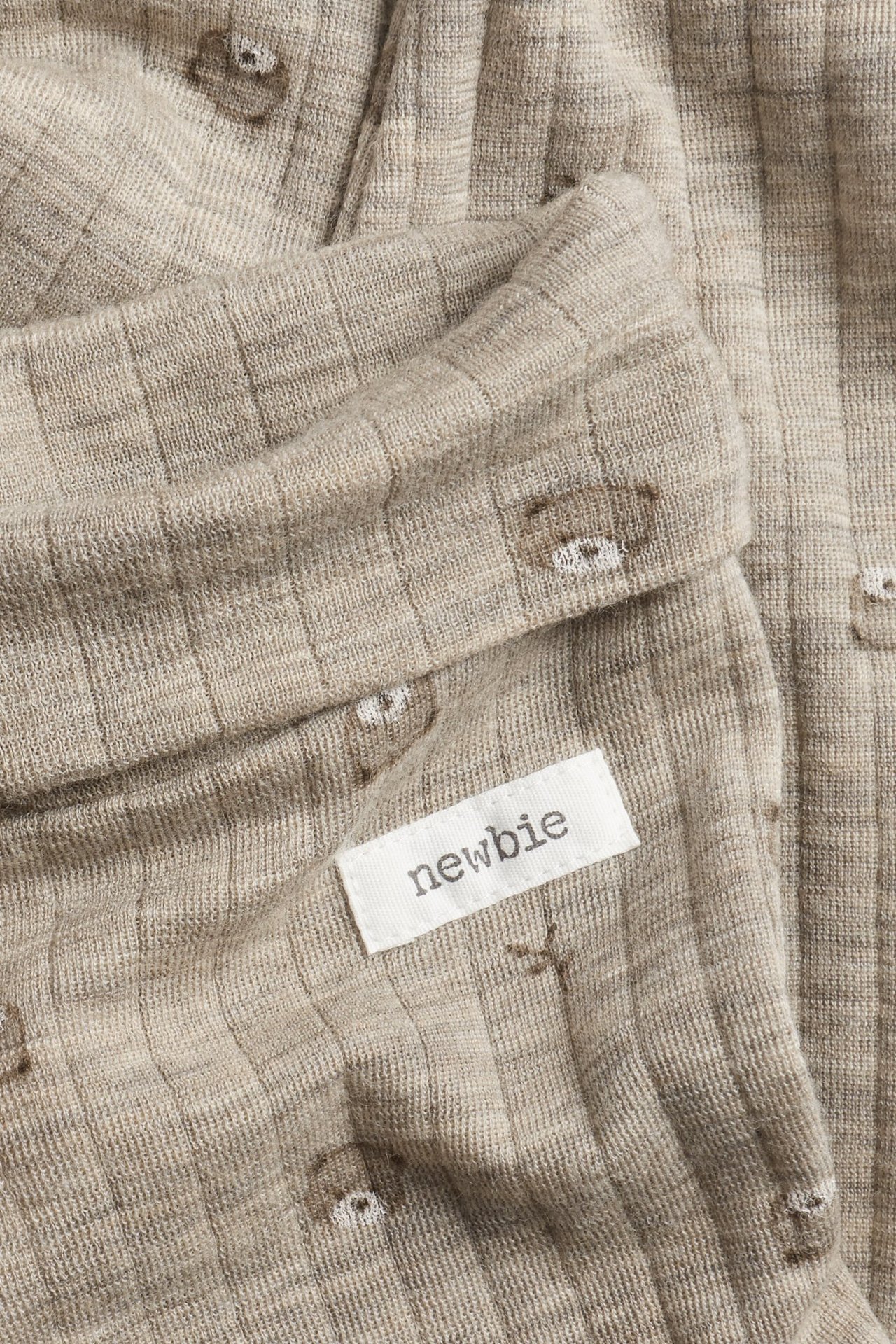 Närbild av beigemelange ribbade ullleggings för baby med nallemönster och Newbie-etikett.