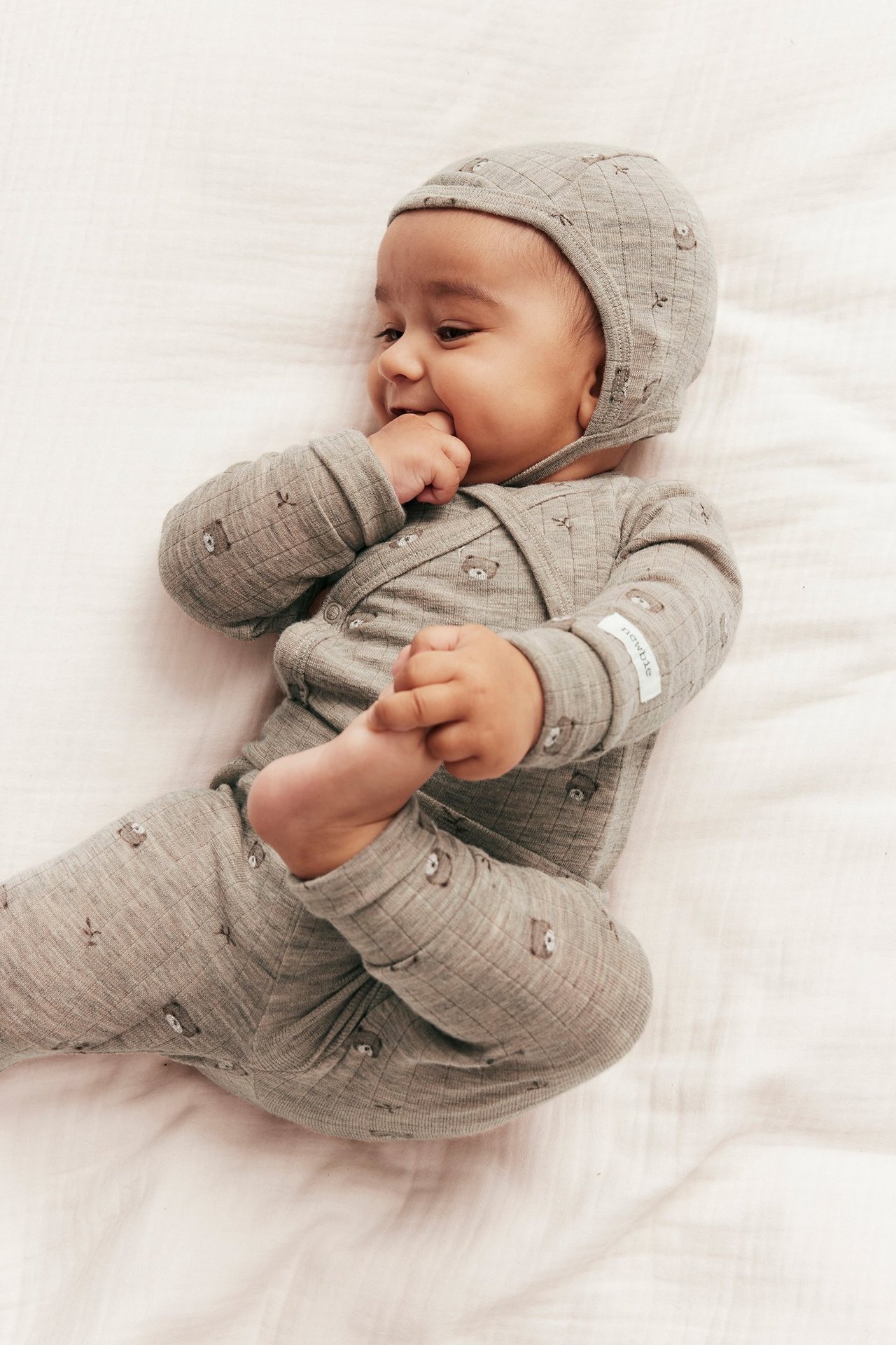 Baby i en beige melerad ribbad ullbody med nallemönster och matchande mössa.