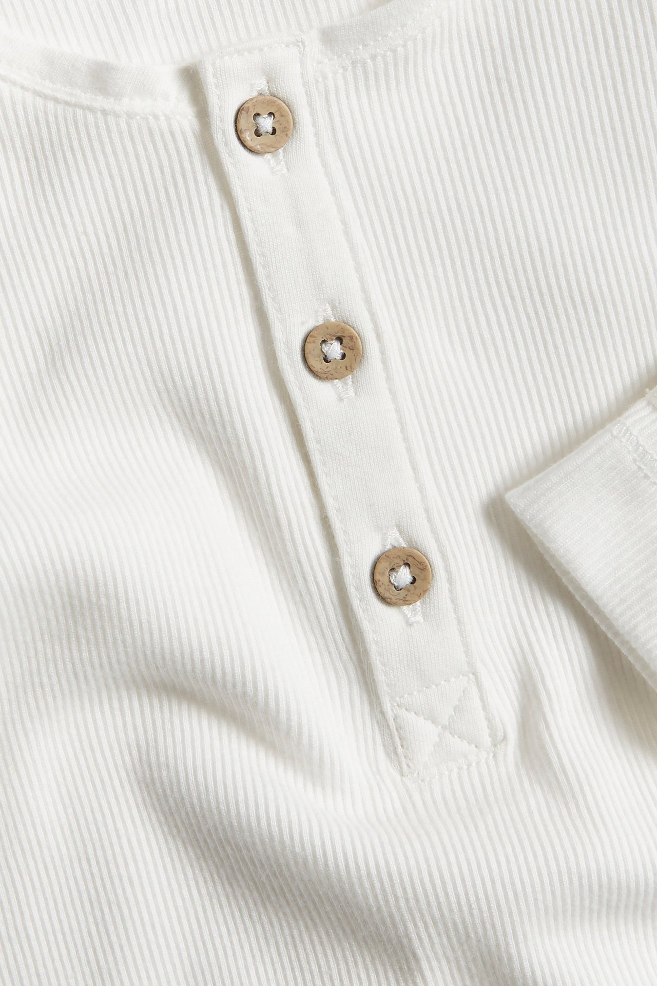 Zbliżenie białego prążkowanego bawełnianego body niemowlęcego z listwą i trzema drewnianymi guzikami.