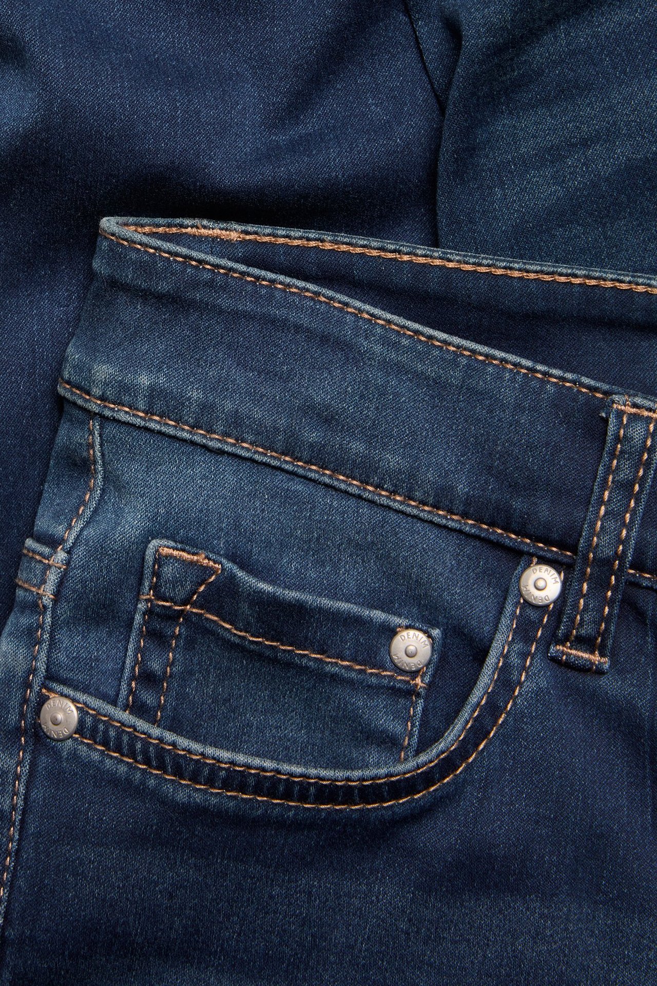 Zbliżenie na ciemnoniebieskie jeansy Super Slim High Waist, przednia kieszeń z brązowymi szwami i srebrnymi nitami.