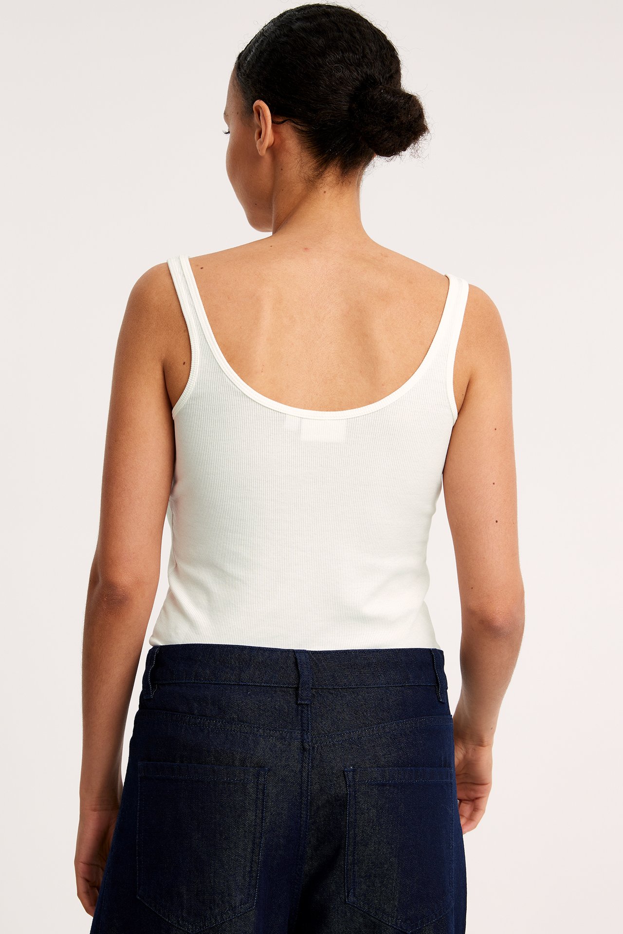 Bakifrån: en kvinna i ett offwhite ribbat linne och mörkblå jeans.
