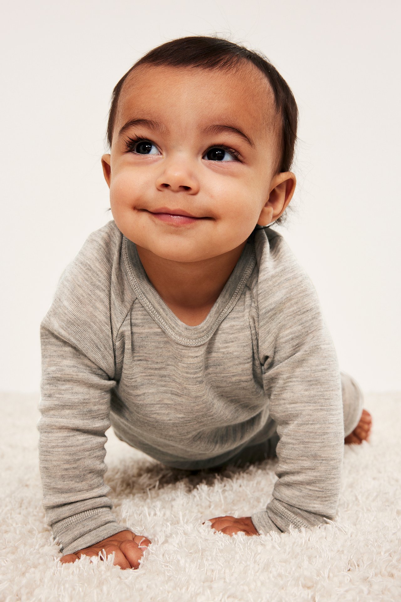 Frontbilde av en krabbende baby i en melert beige merinoull undertrøye og matchende underdeler.