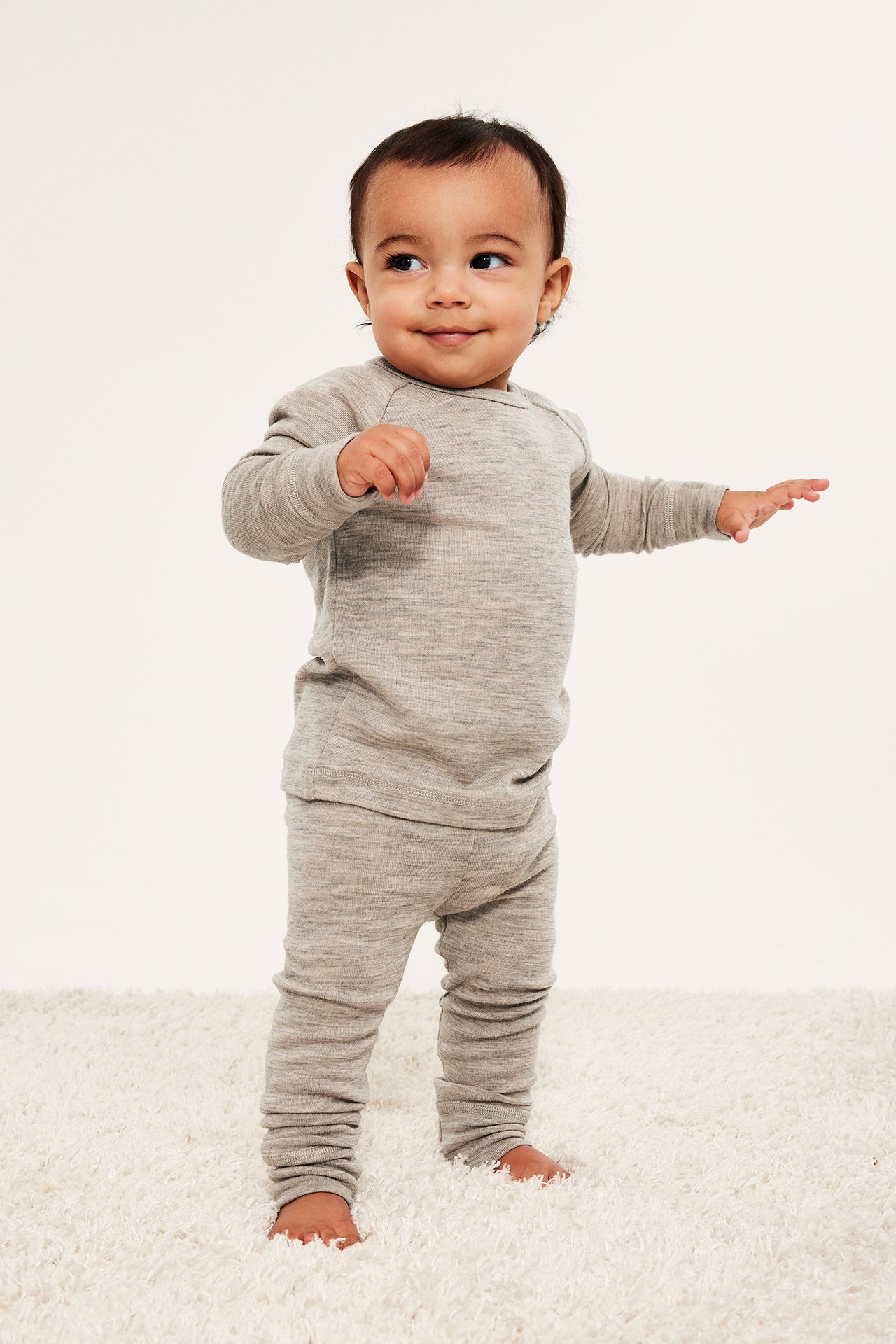 Widok z przodu: niemowlę w dopasowanym, beżowym melanżowym zestawie bielizny z wełny merynosów.