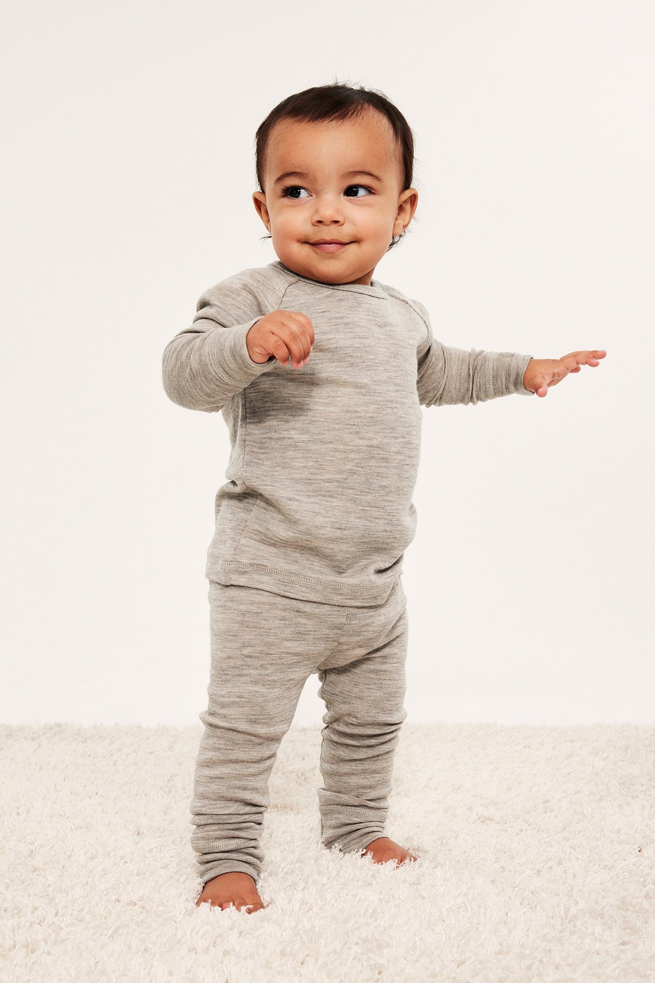 Frontvy av en baby i ett åtsittande, melerat beige underställ i merinoull.