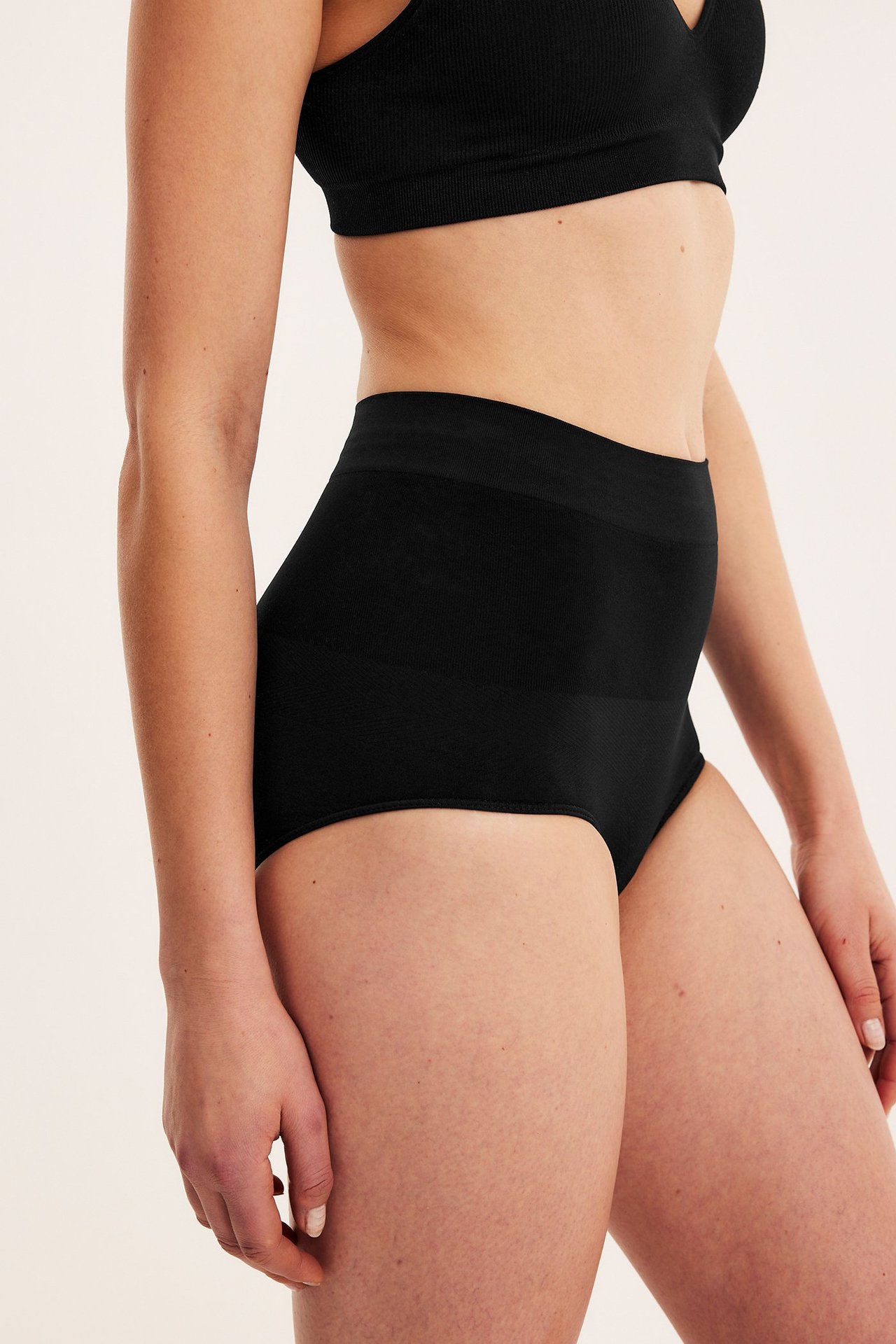 Sidovy av en kvinna i svarta sömlösa shapingtrosor med hög midja och en svart ribbad BH.
