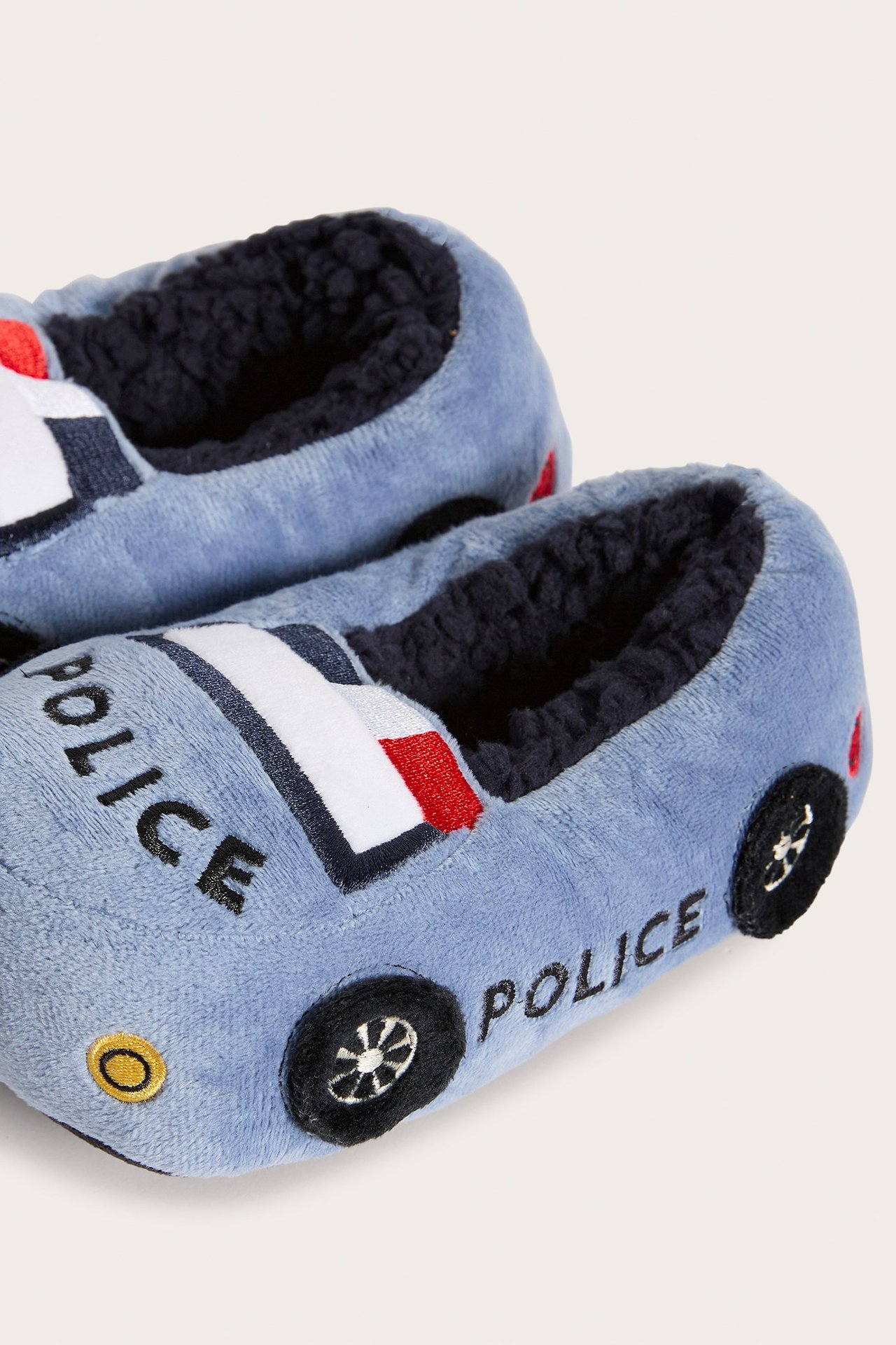 Lähikuva sinisistä lasten poliisiauto-tohveleista, joissa musta "POLICE"-teksti ja tumma fleecevuori.