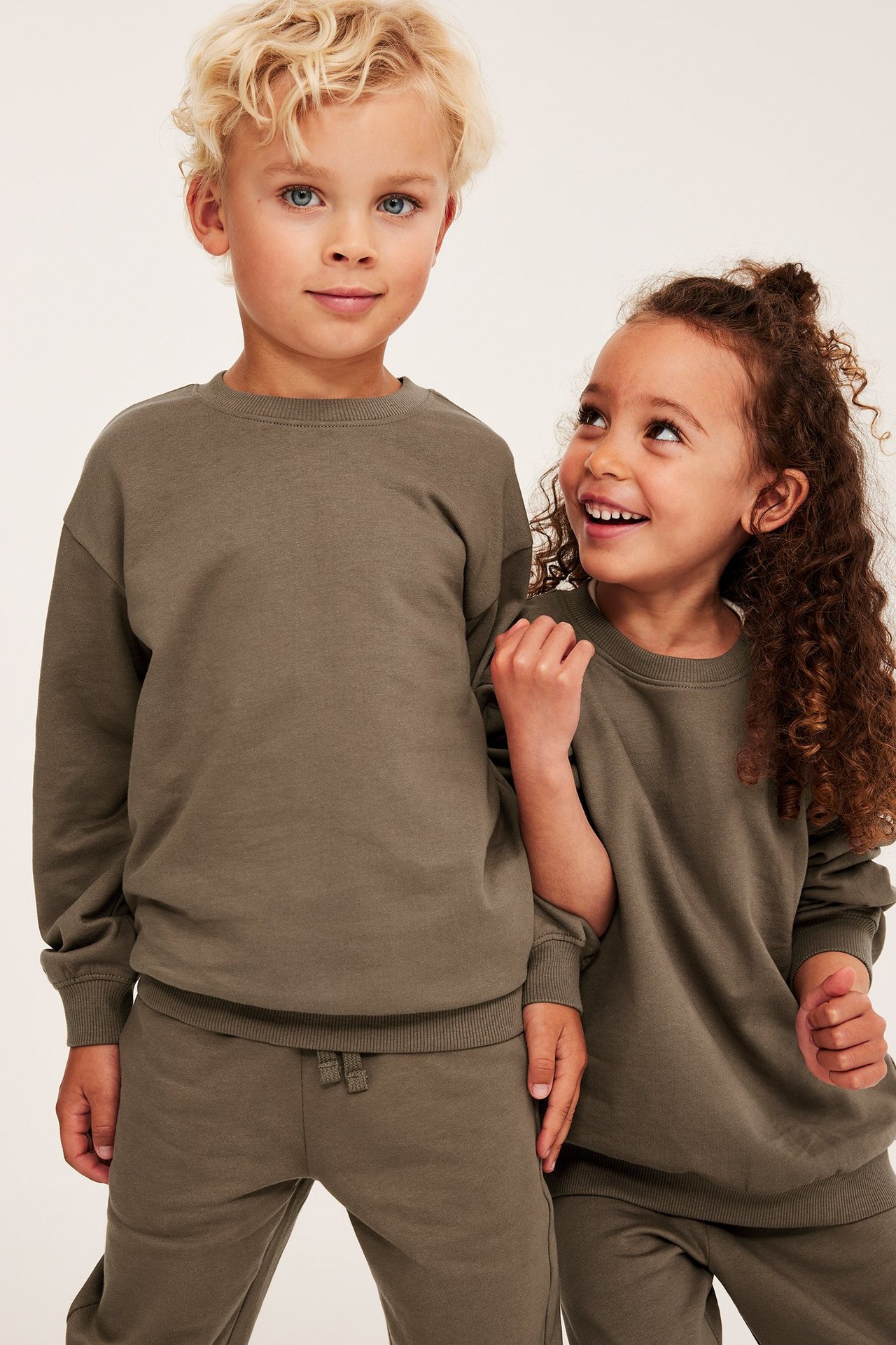 Edestäpäin, poika ruskeassa puuvillapaidassa ja yhteensopivissa collegehousuissa, tyttö samanlaisessa asussa.