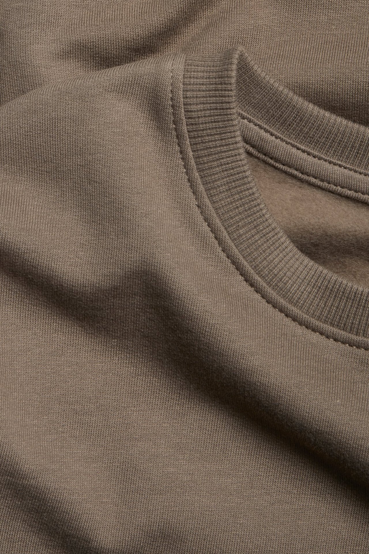 Zbliżenie na brązową, jednolitą bawełnianą bluzę z okrągłym, prążkowanym dekoltem.