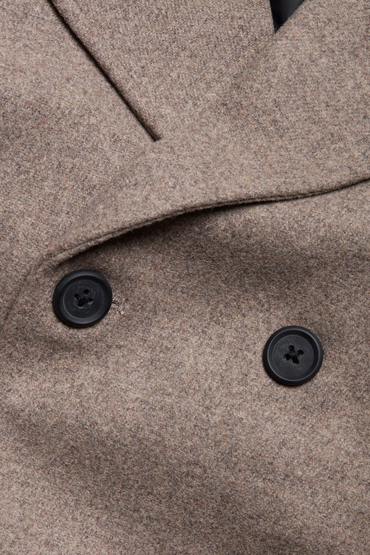 Zbliżenie beżowej melanżowej kurtki z dwoma czarnymi guzikami.