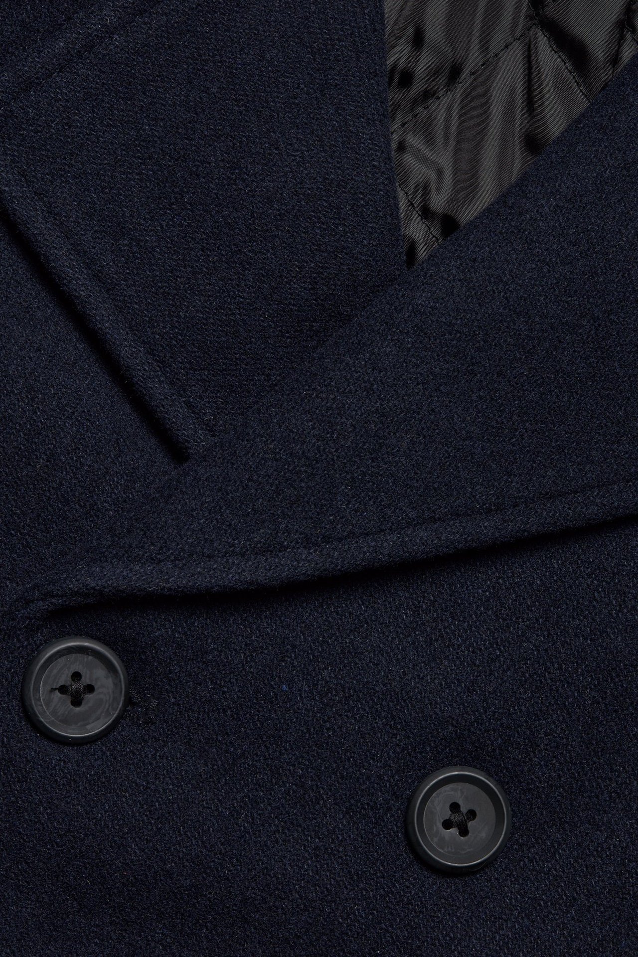 Zbliżenie: granatowy melanżowy płaszcz marynarski, dwa ciemne guziki, czarna pikowana podszewka.