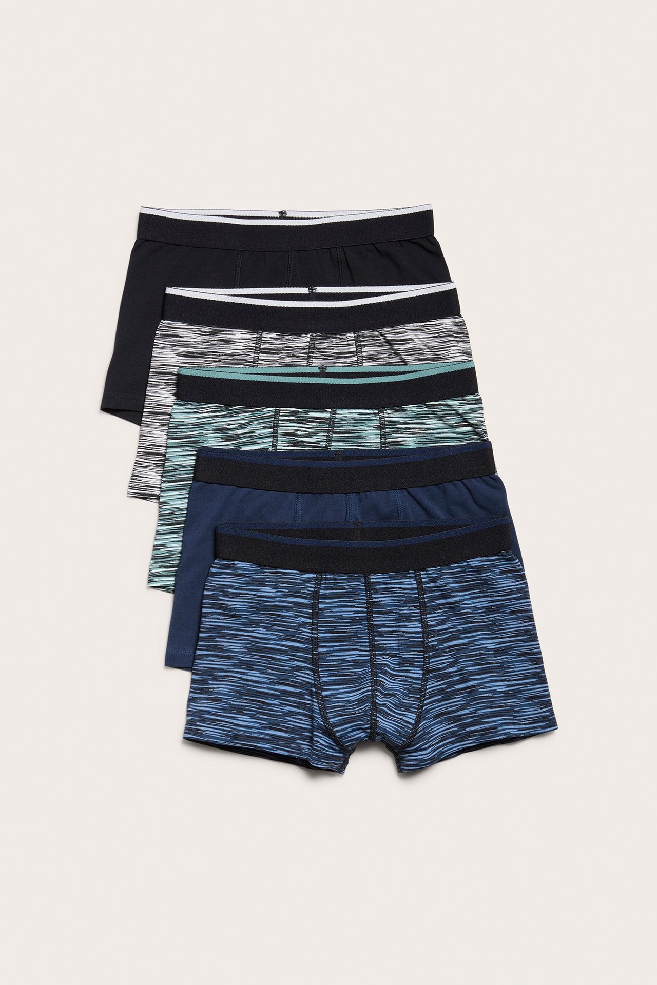 Widok z przodu pięciu par bokserek dziecięcych: dwie jednolite czarne/granatowe, trzy wzorzyste w szarości, mięcie i błękicie.