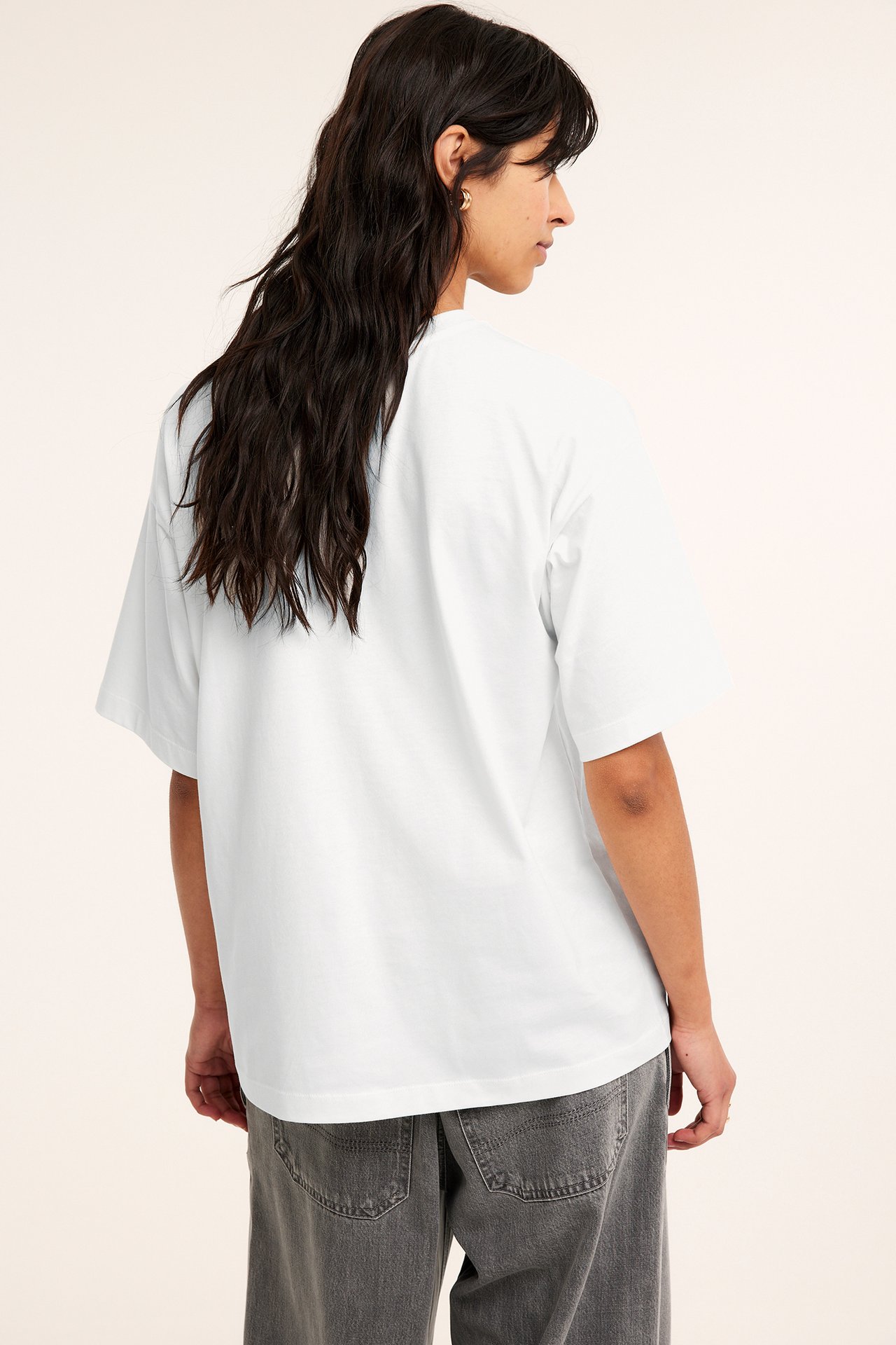Ryggvisning av en kvinne i en offwhite oversized bomulls-t-skjorte og mørkegrå jeans.